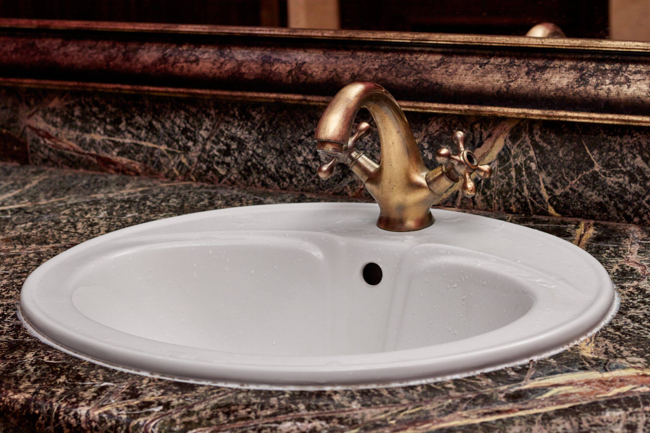 A closeup of a brass faucet with hot and cold handles on a white lavatory sink in a restroom