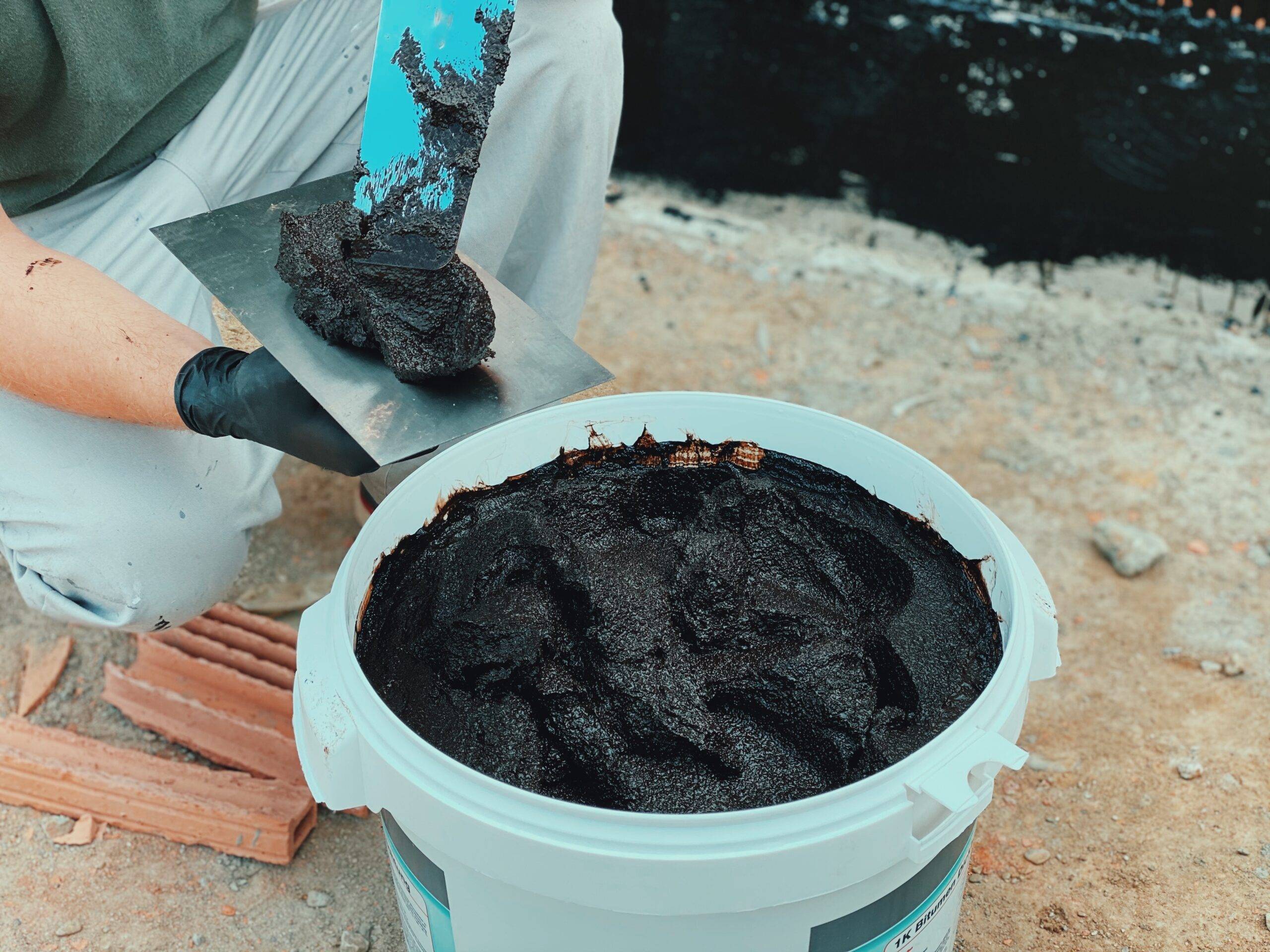 A person scooping mortar from a bucket onto a spreader.