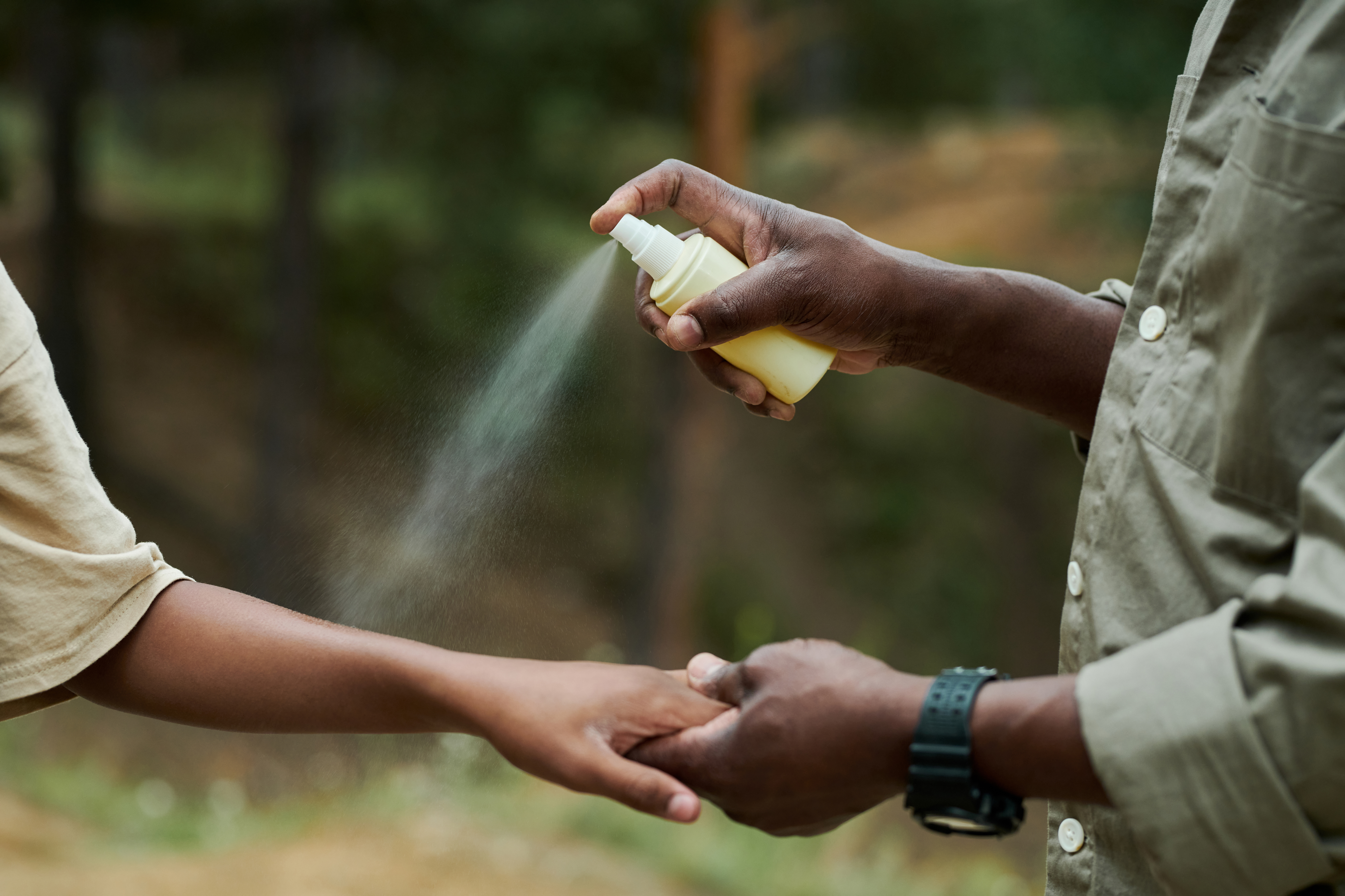 Close-up of African American dad spraying the hand of his son with mosquito spray during hiking
