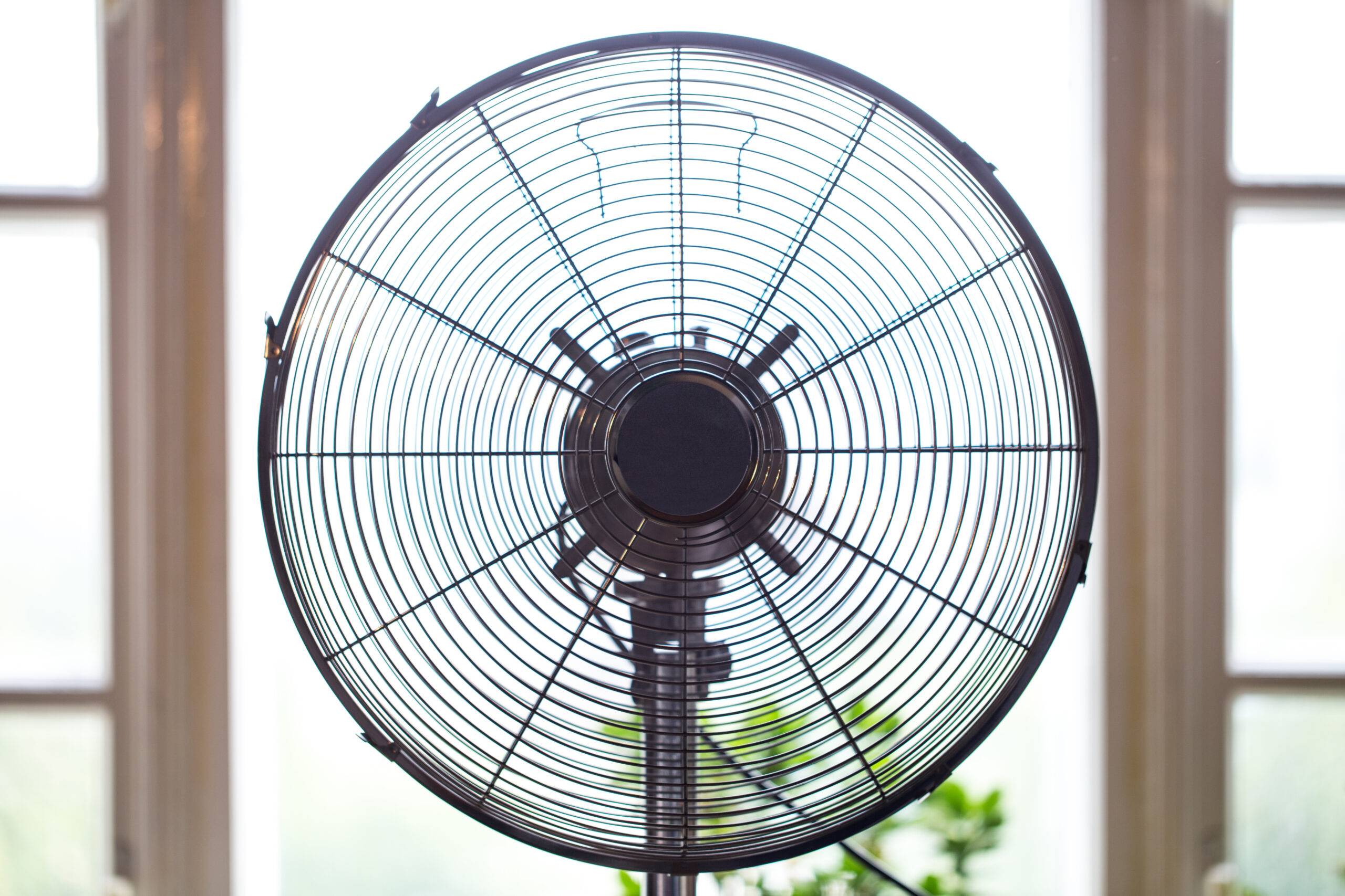 Electric fan in front of a window, close up.