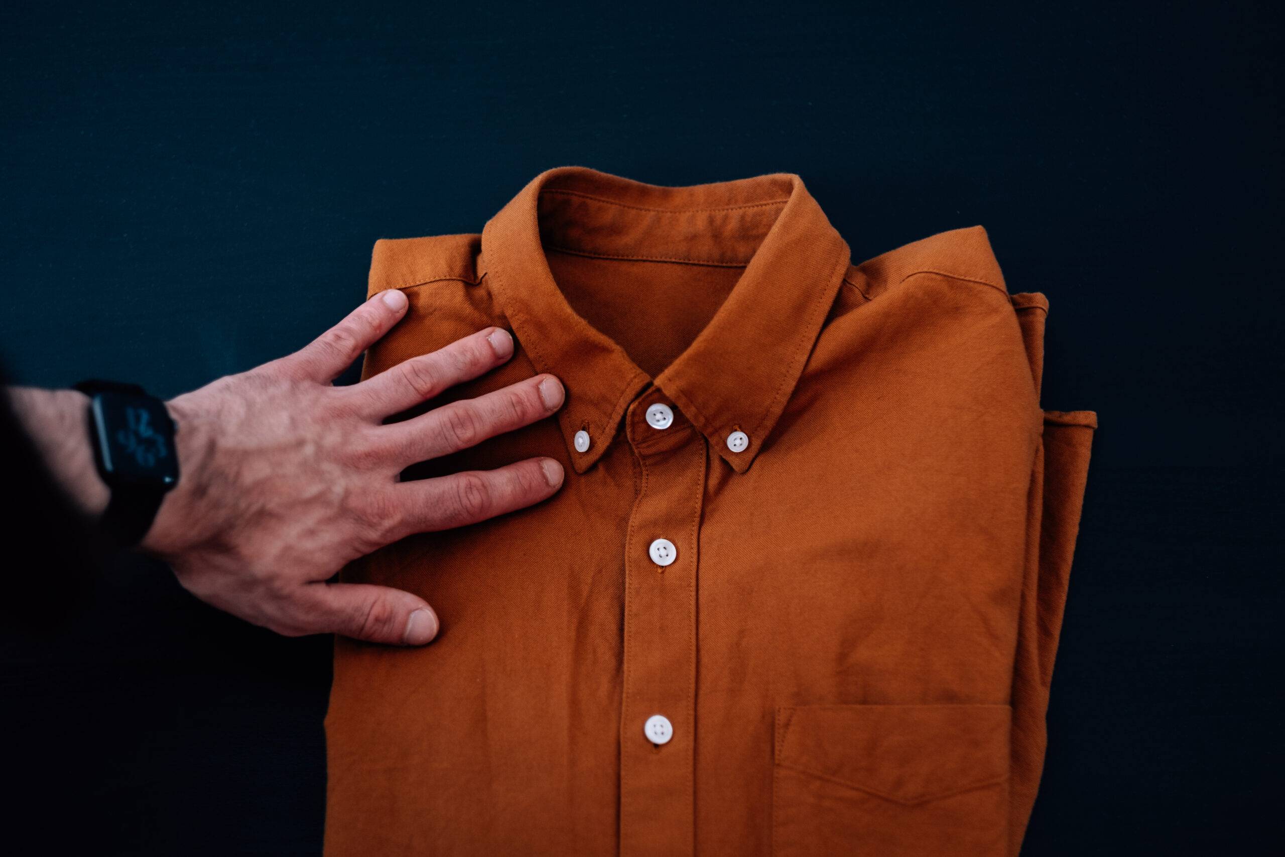 A male's hand wearing a smartwatch touching a folded brown shirt