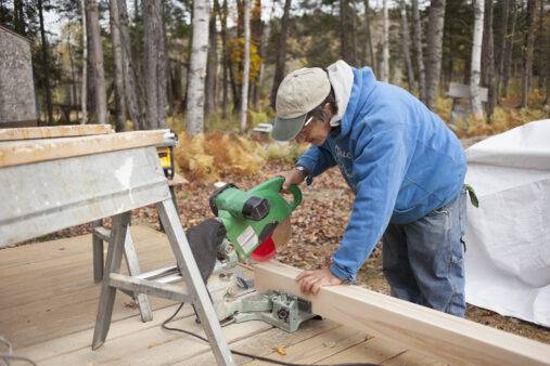 Mature man sawing plank of wood outside house