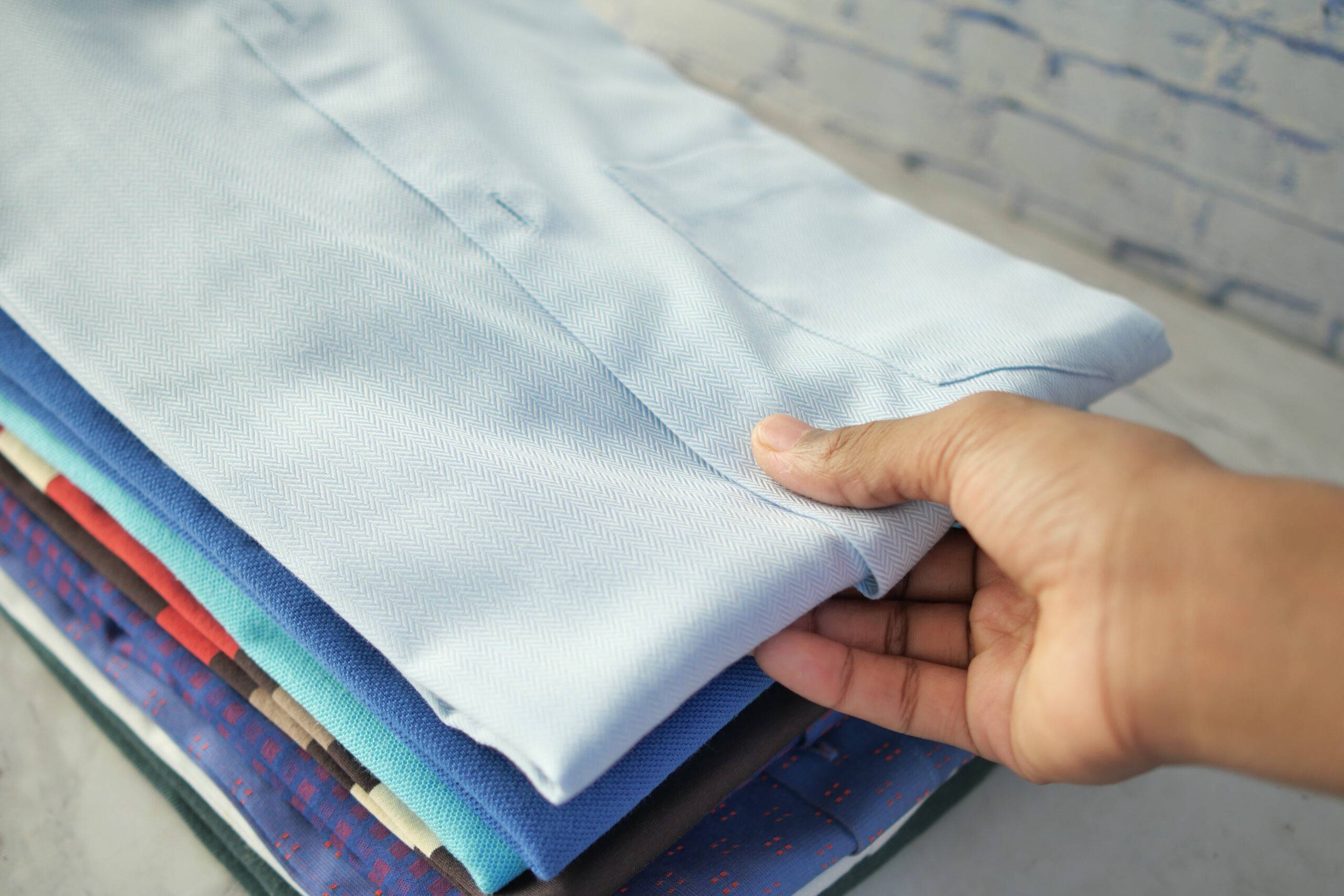 A stack of folded men's button up shirts, a hand reaching out to grab the first one.
