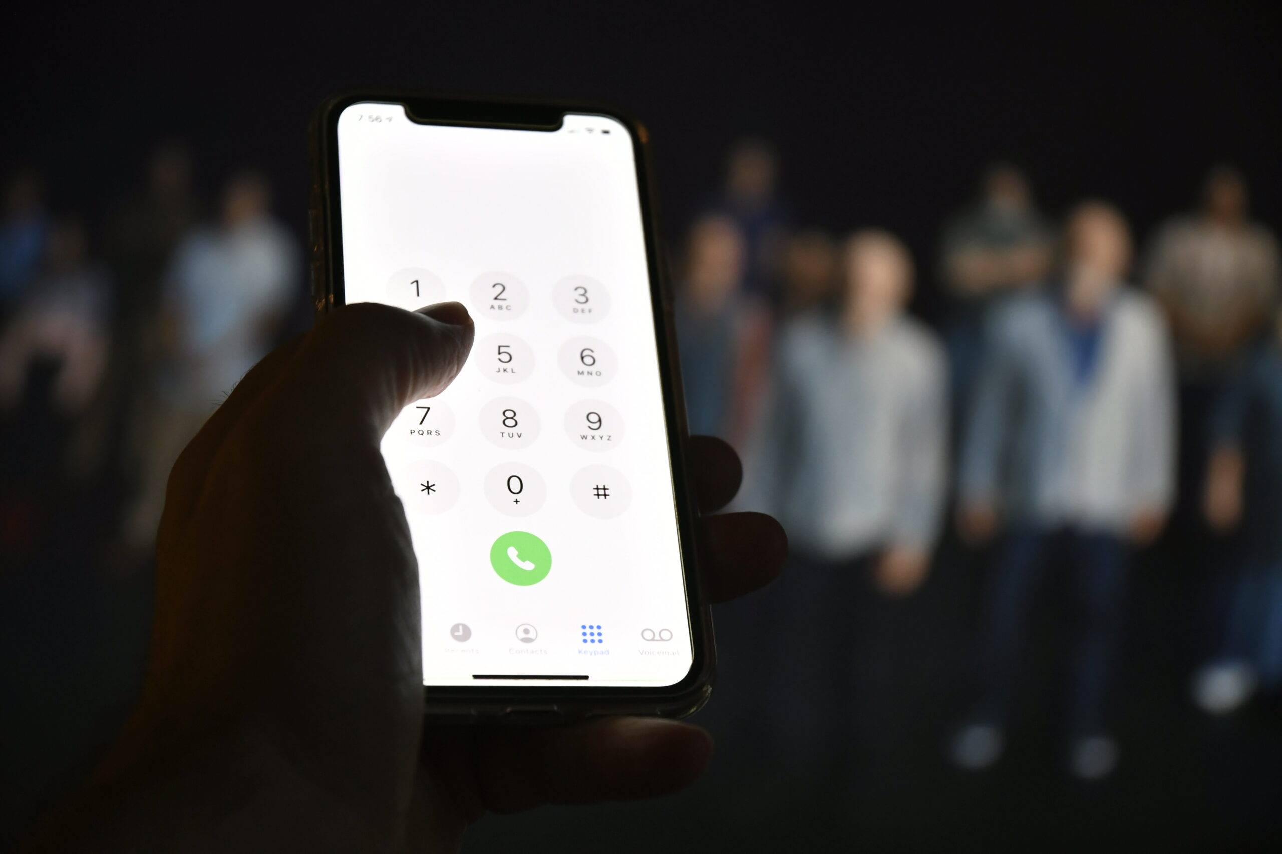 A hand holding a phone that's opened to the dial screen, a blurred out crowd of people in the background.