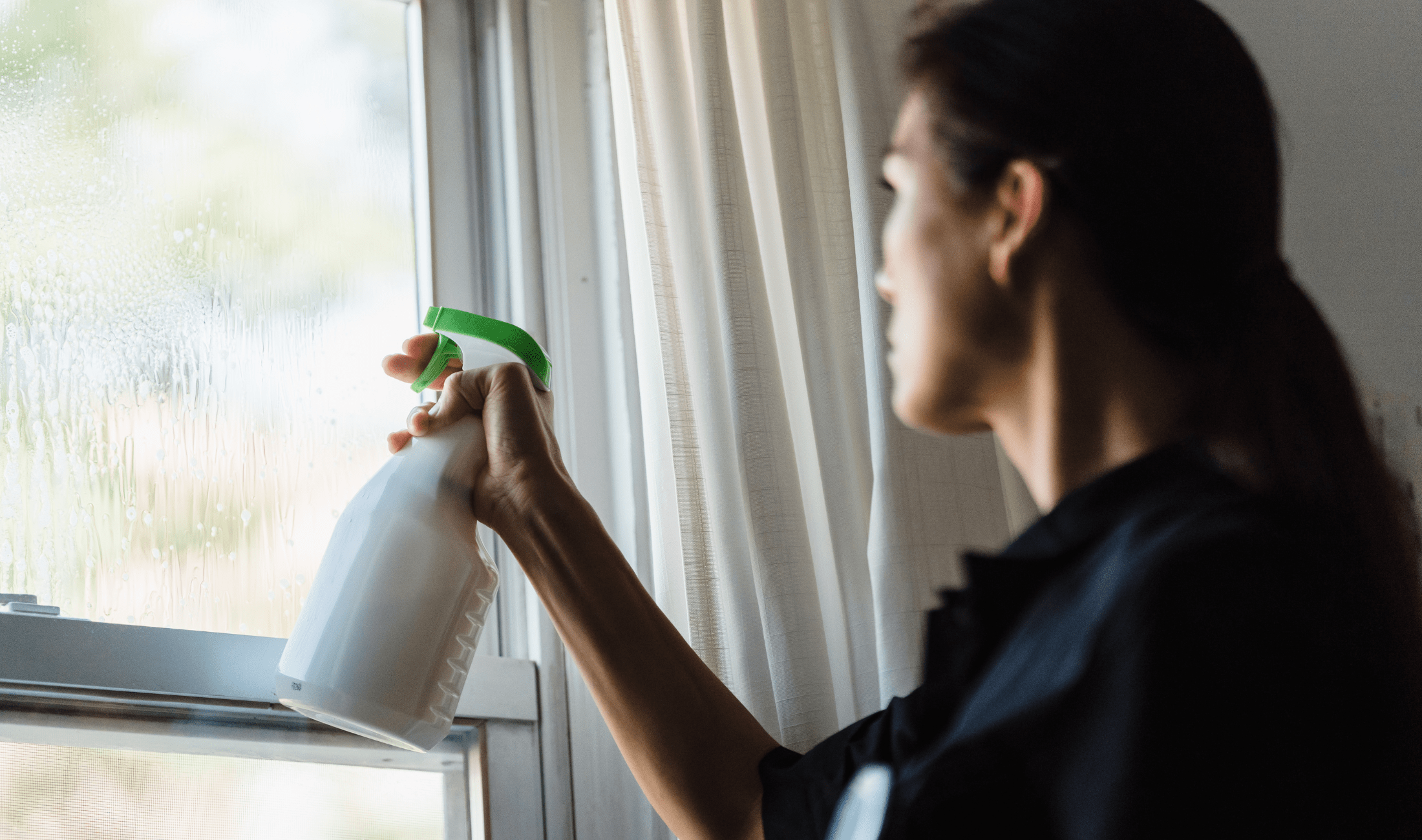 A woman using a spray bottle of cleaner on her windows.