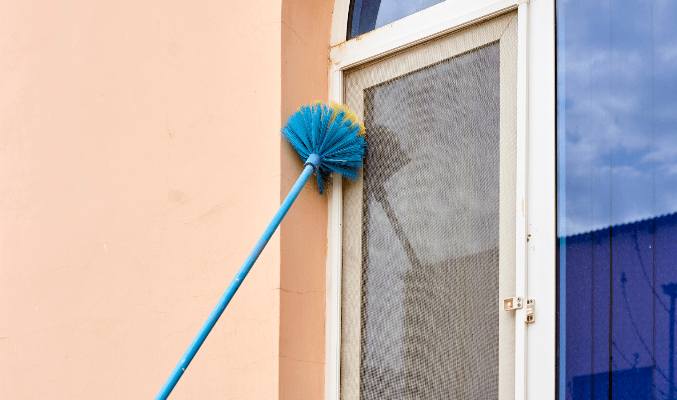 A person using a dry brush to clean the outside frame of a window.
