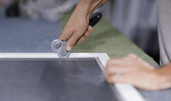 Someone using a tool to fit window screens.