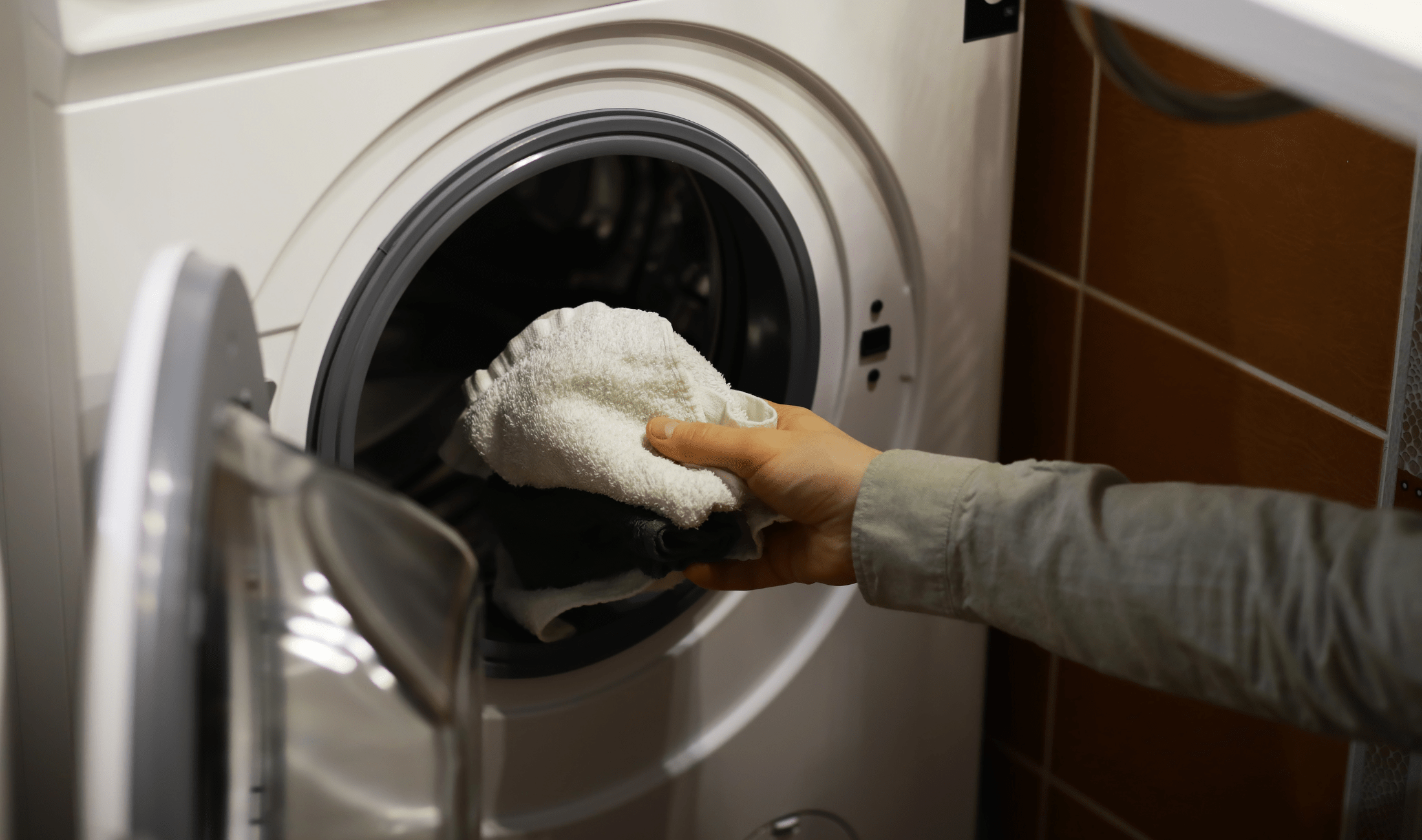 A person reaching out to put a towel in a front-loading washing machine.