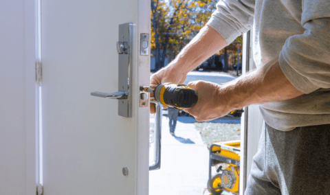 A man using a drill on a door's strike plate.