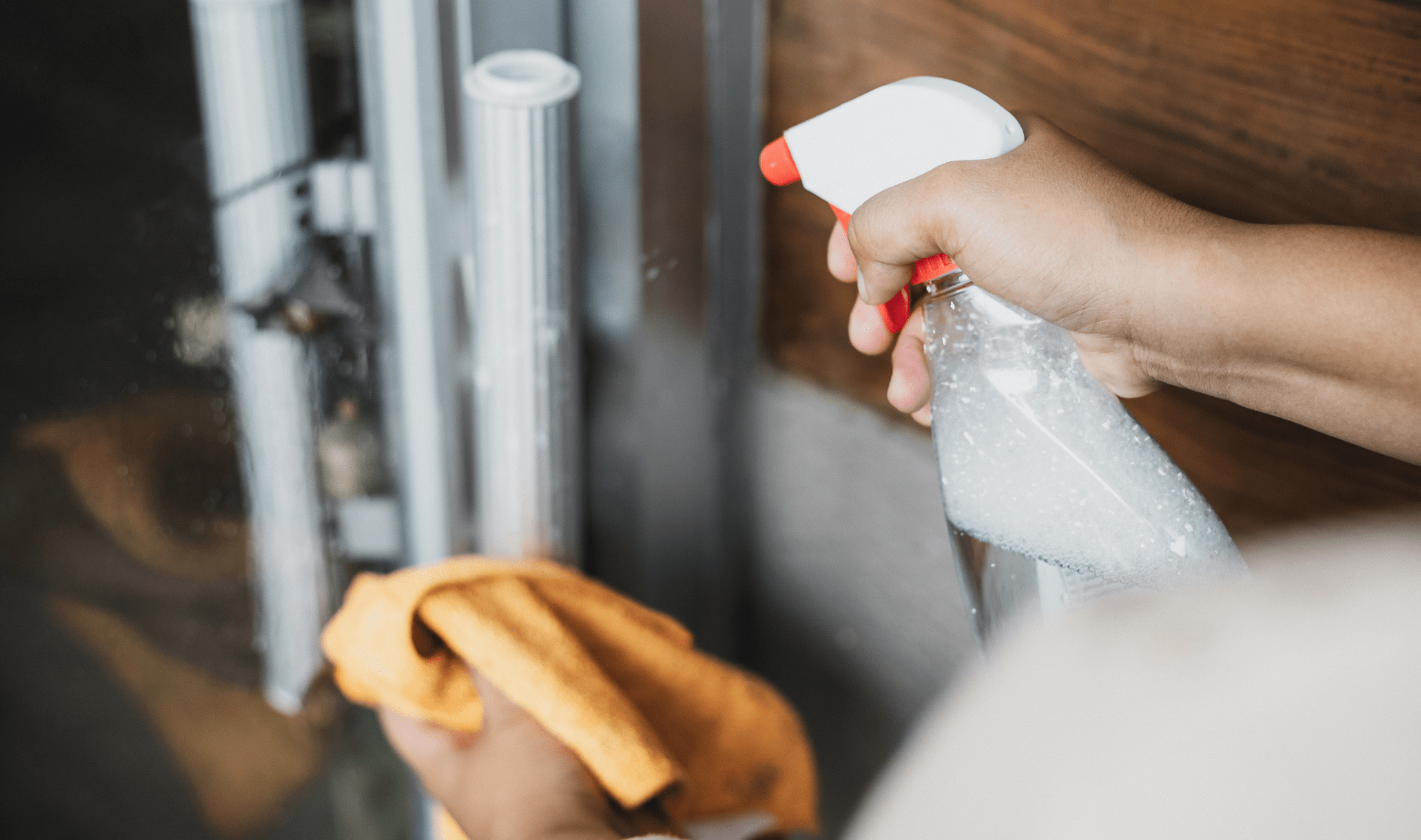 A person using a cleaning solution in a spray bottle to clean a door handle.