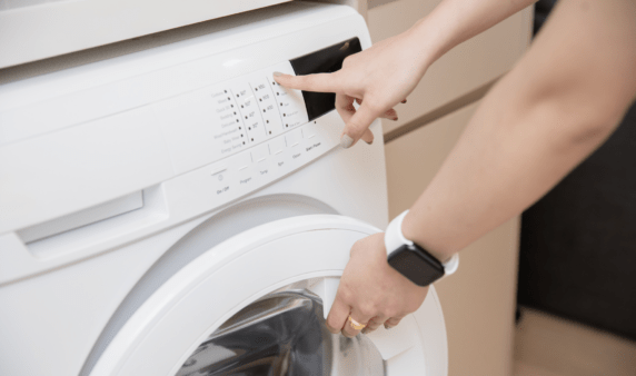 Hands reaching out to close a front-loading washing machine door and press 'start'.