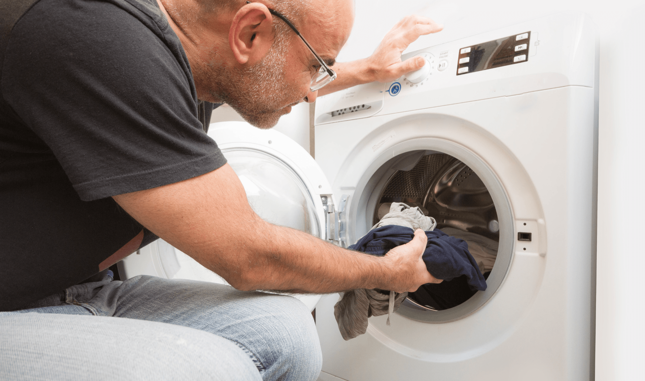 A man putting clothing into a dryer.