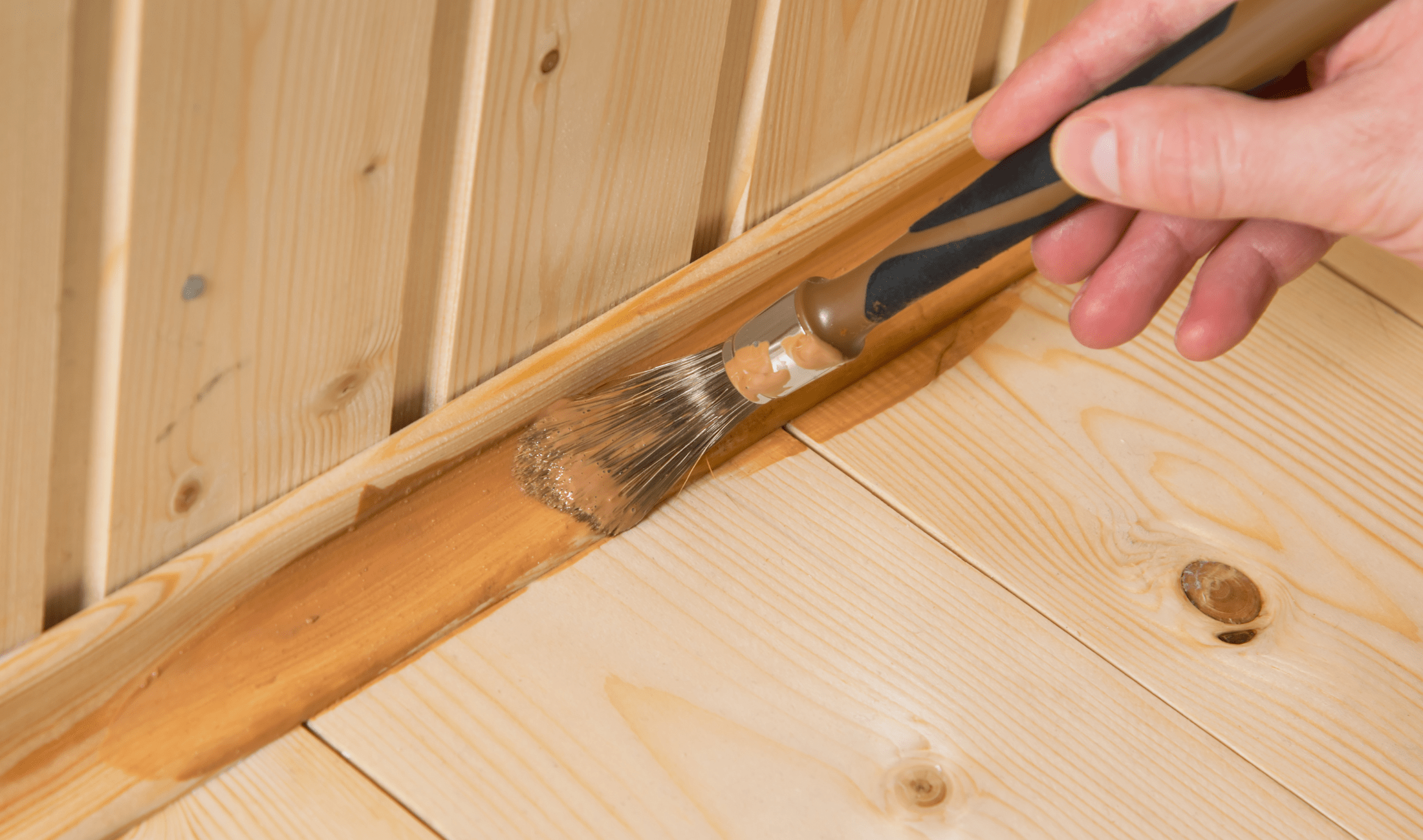 A person staining some wooden baseboards with a specialized brush.