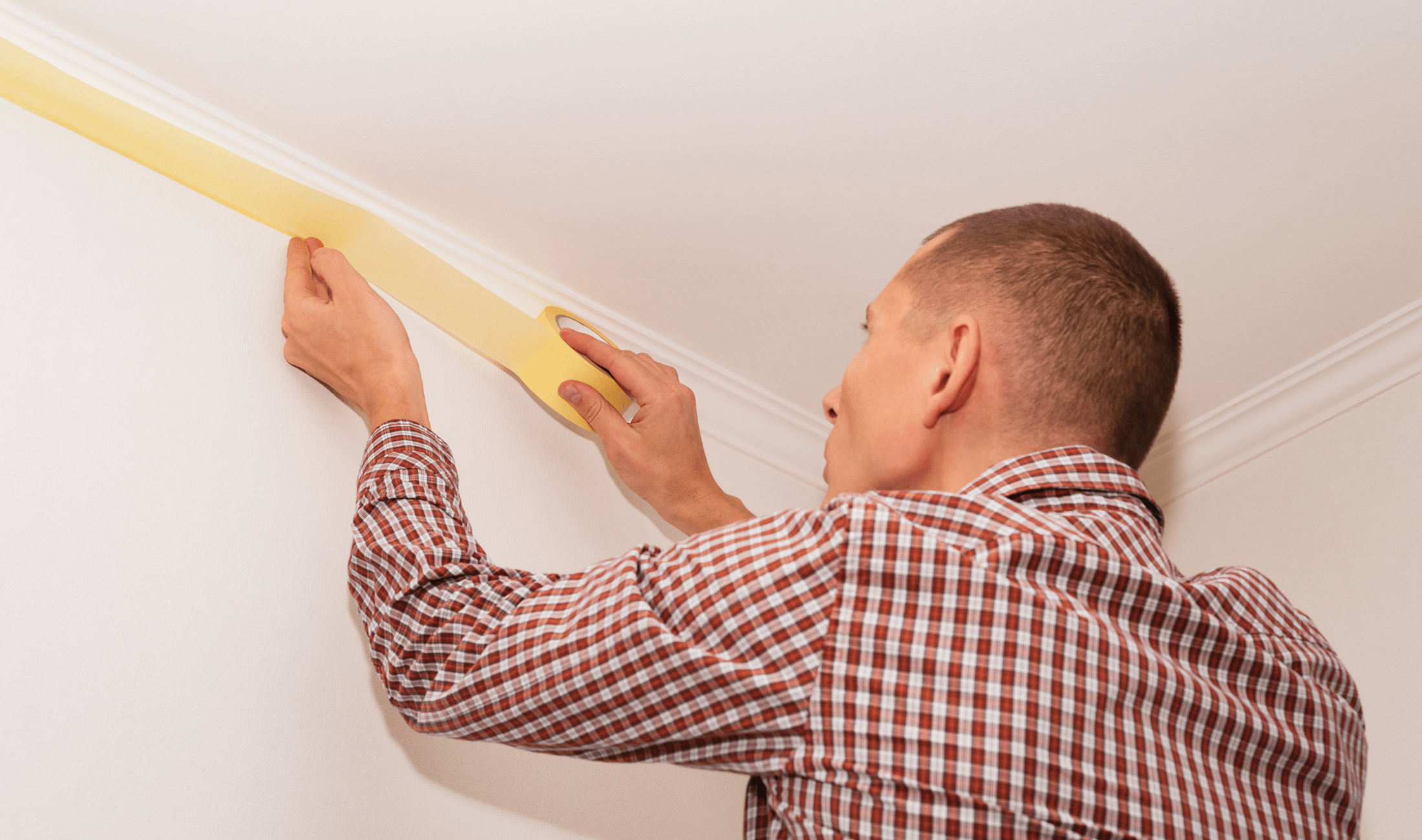 A man using painters tape to line the edges of some crown molding.