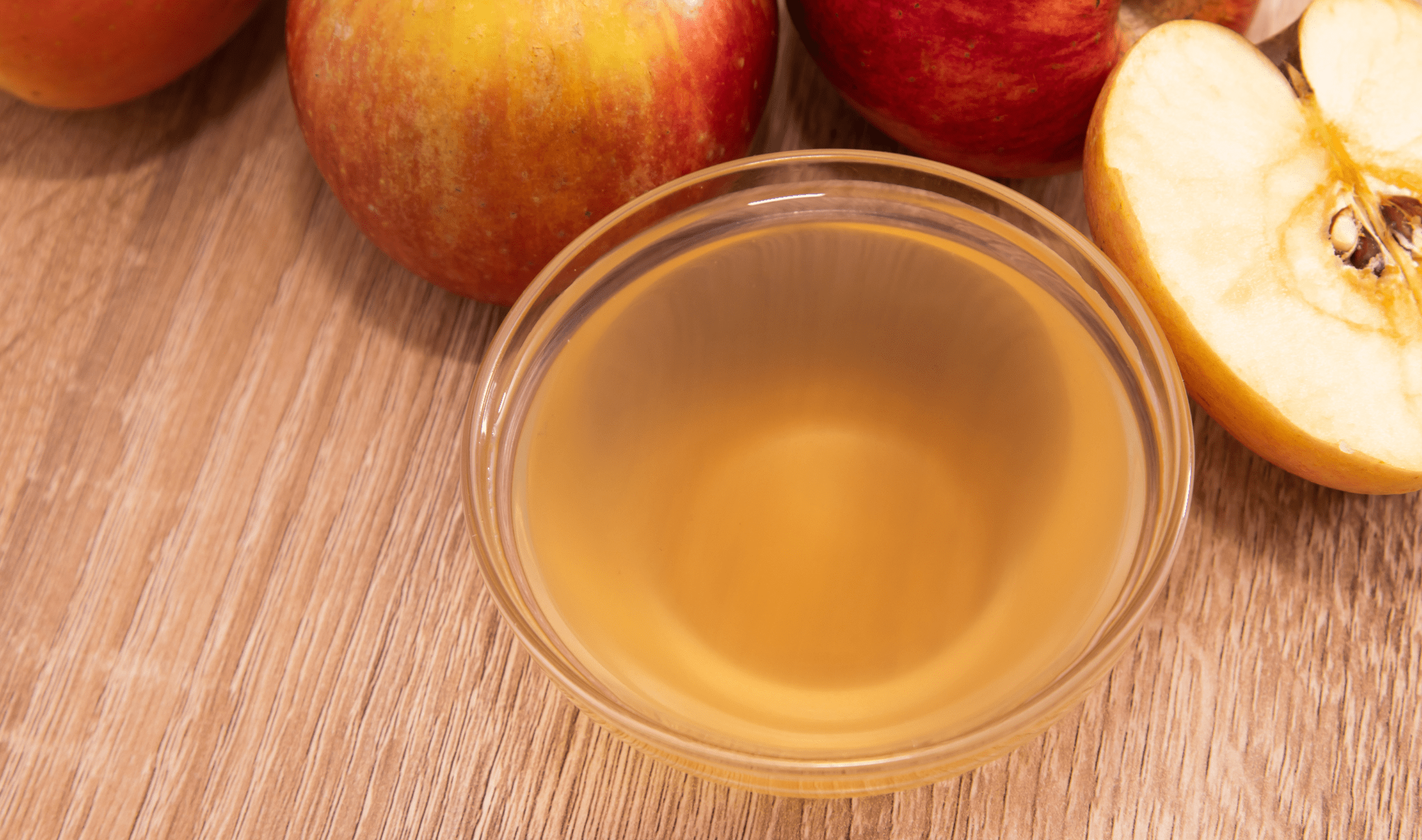 A bowl of apple cider vinegar next to some whole and halved apples.