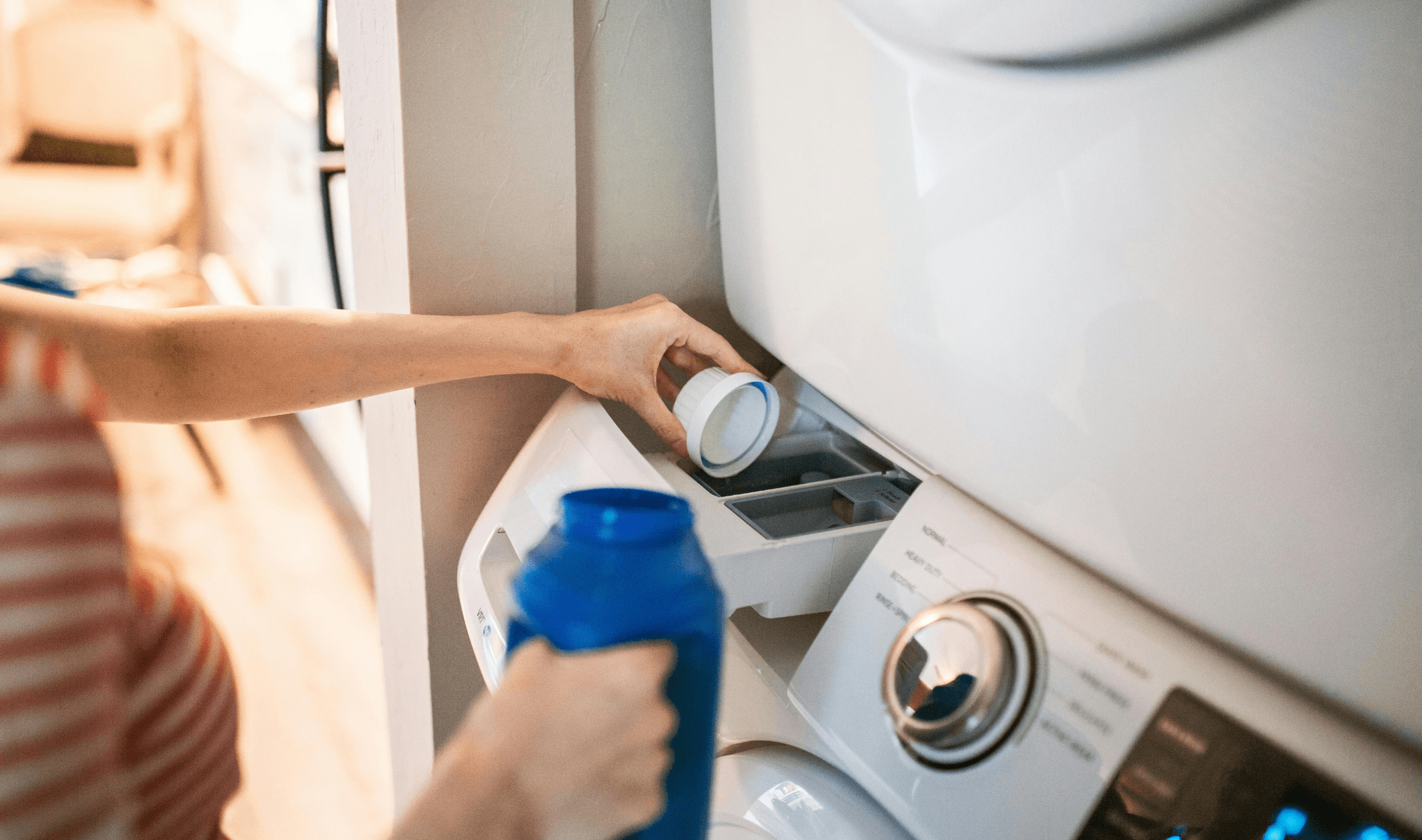 A person putting laundry detergent in the detergent drawer of a washing machine.