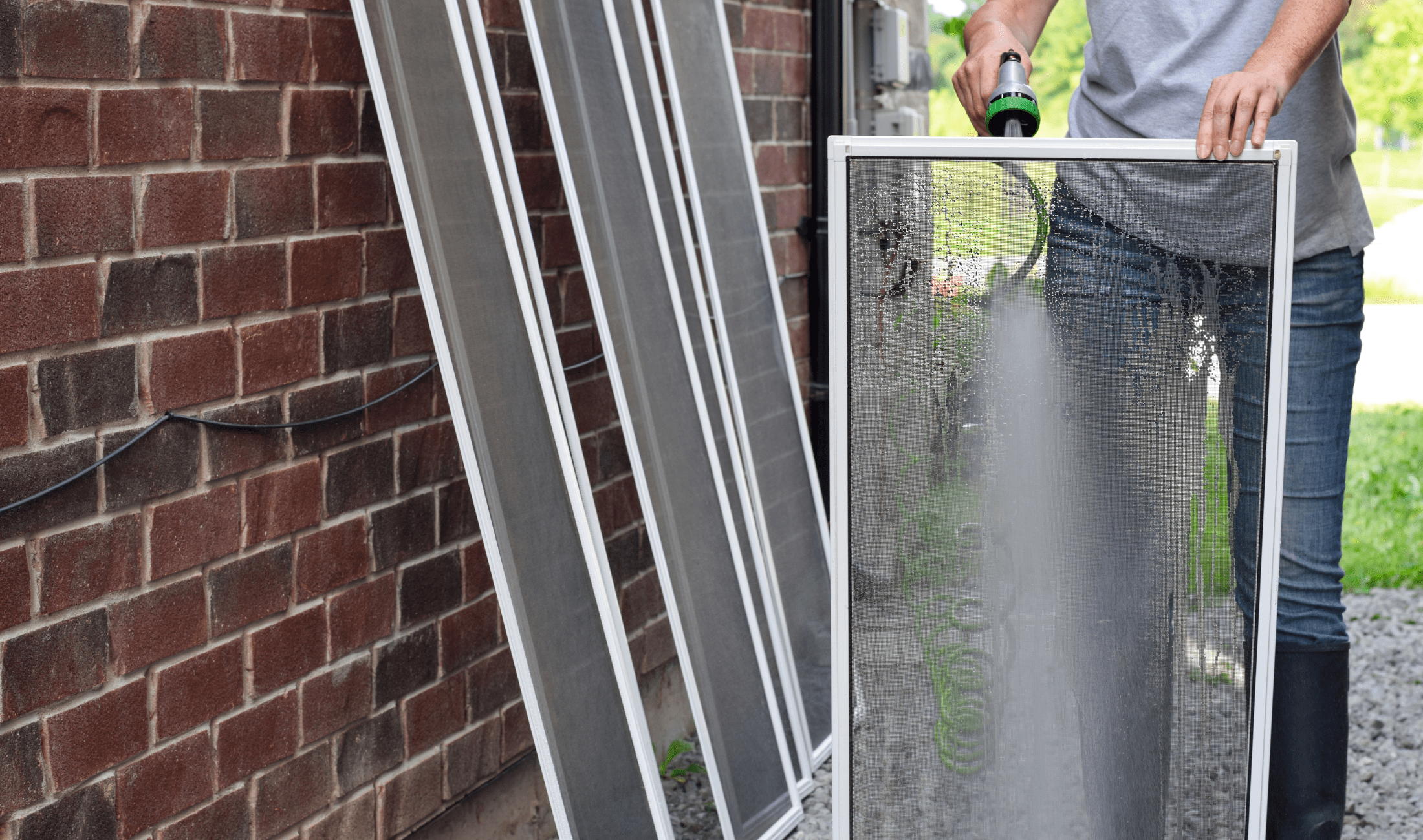 A person washing window screens outside using a hose.