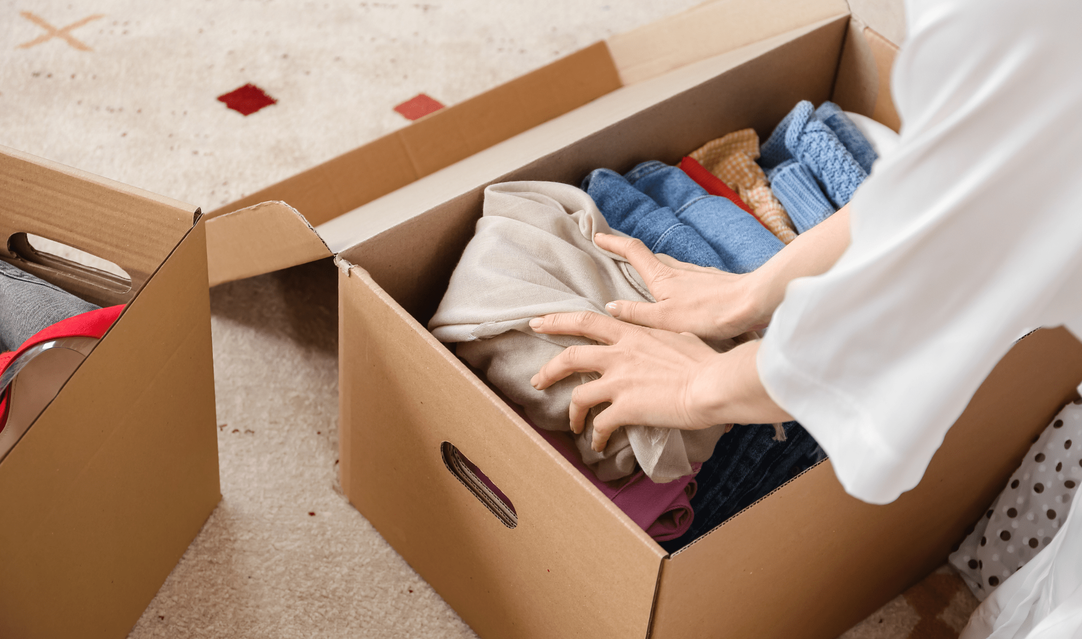 Two hands putting clothes in a cardboard box.