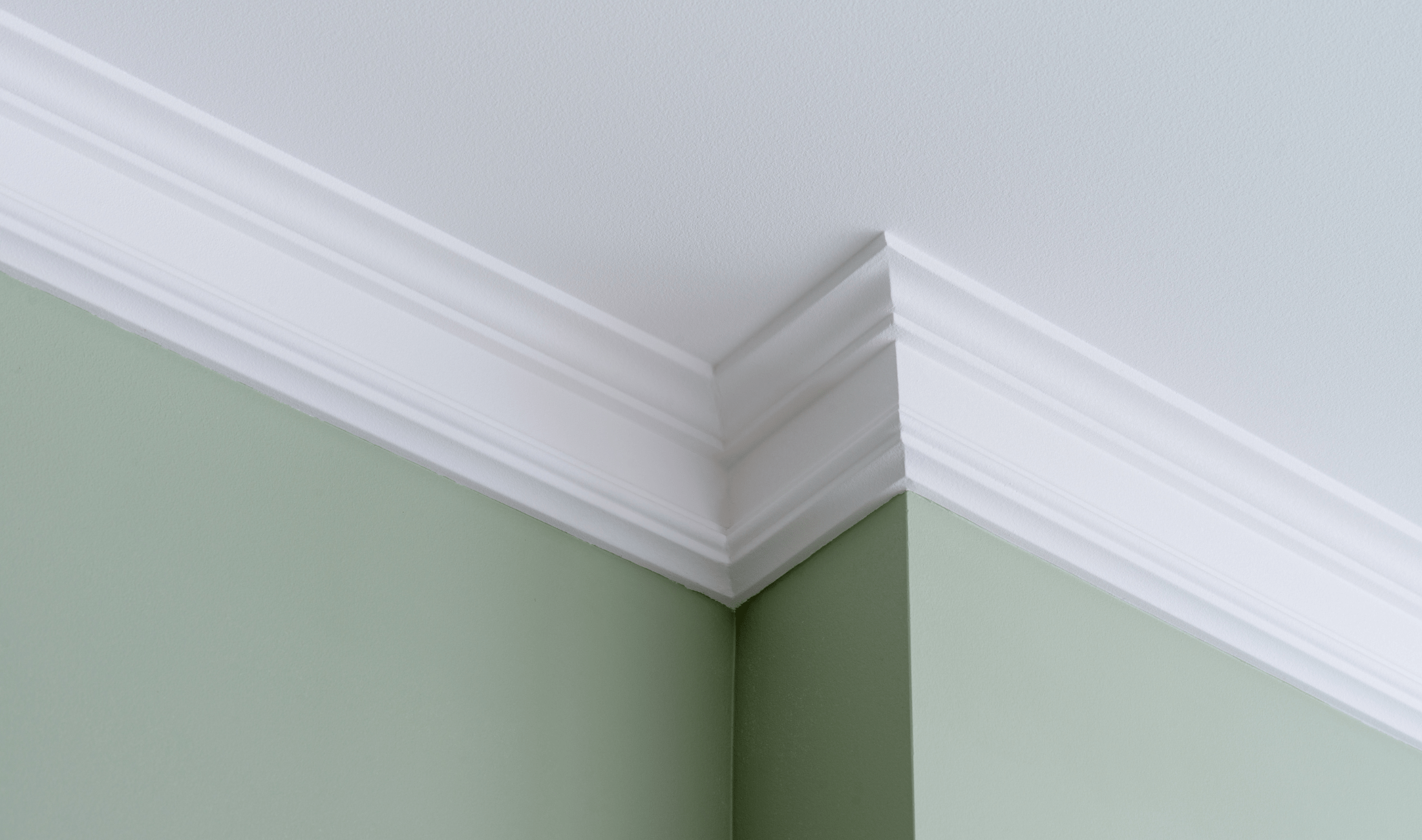 A photo of cleanly painted molding against a sage green wal.