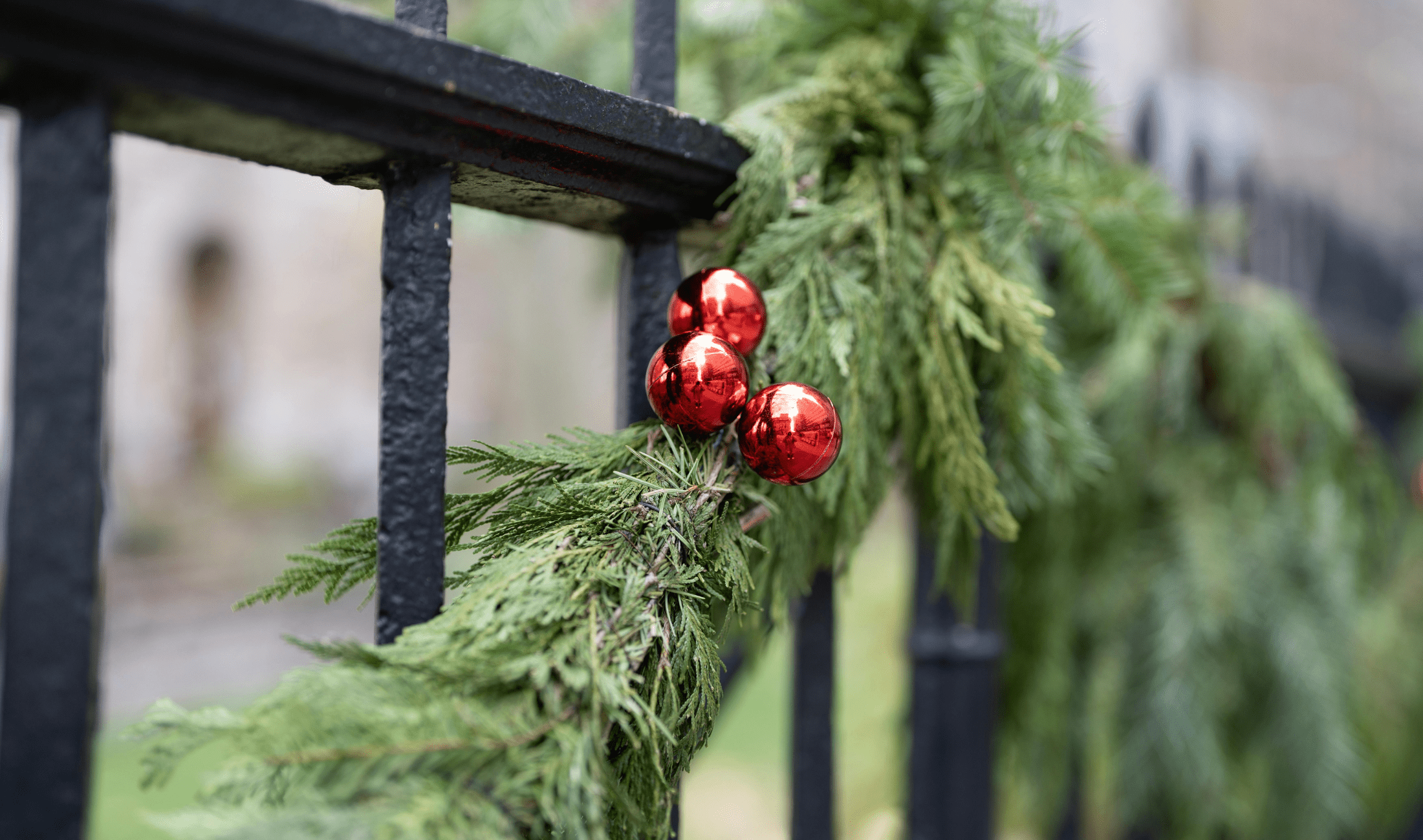A close photo of three red ornaments on a pine garland.