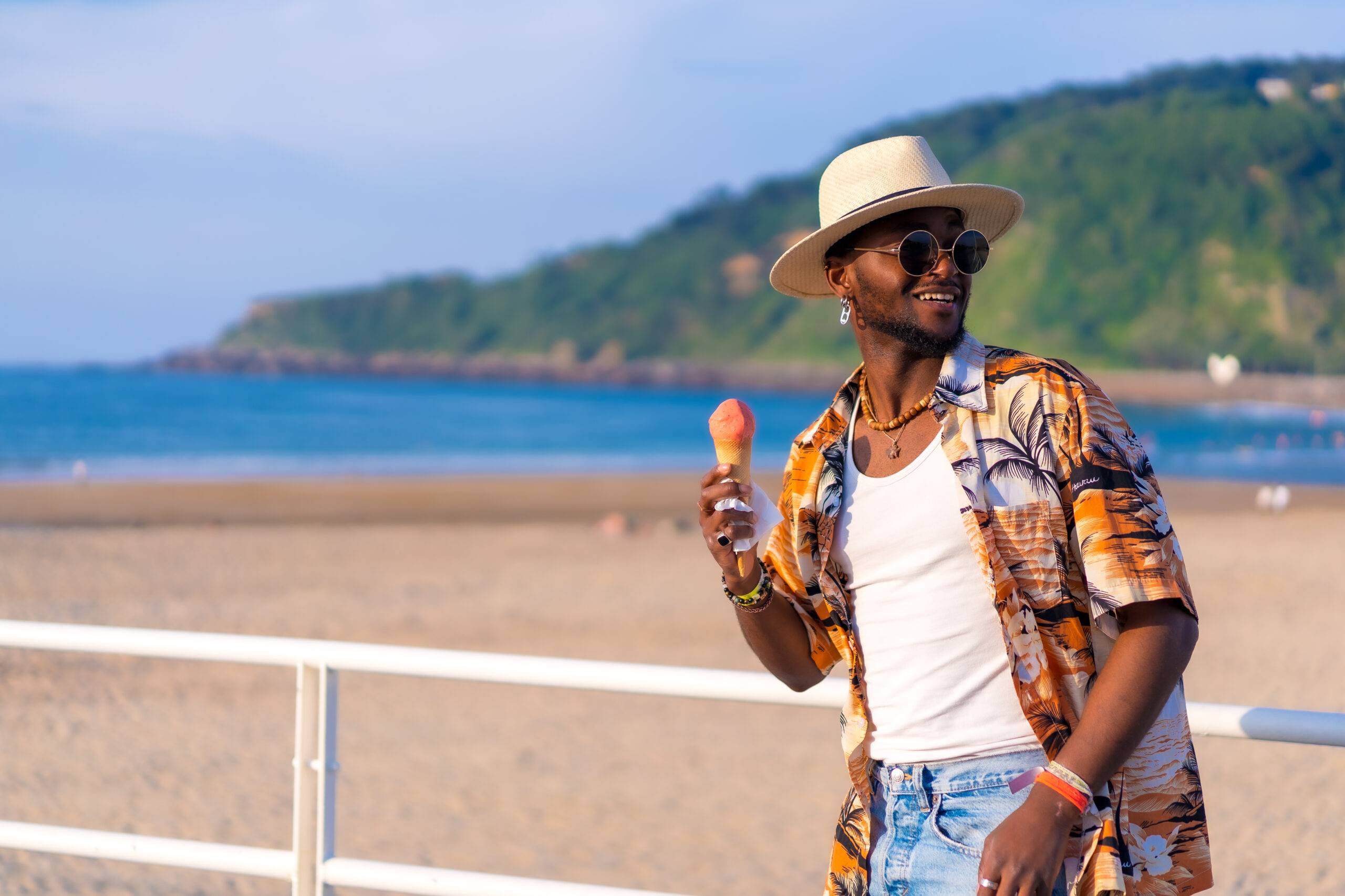 Black ethnic man enjoy summer vacation on the beach eating an ice cream enjoying strolling