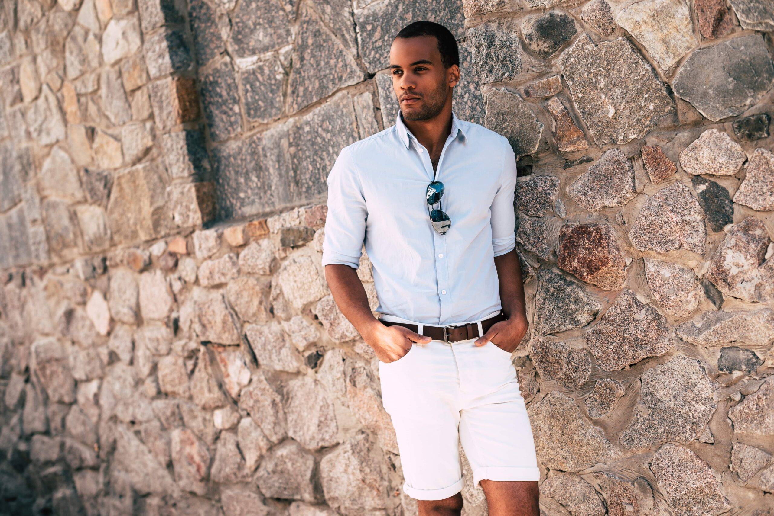A man standing next to a brick wall, hands in his pockets.