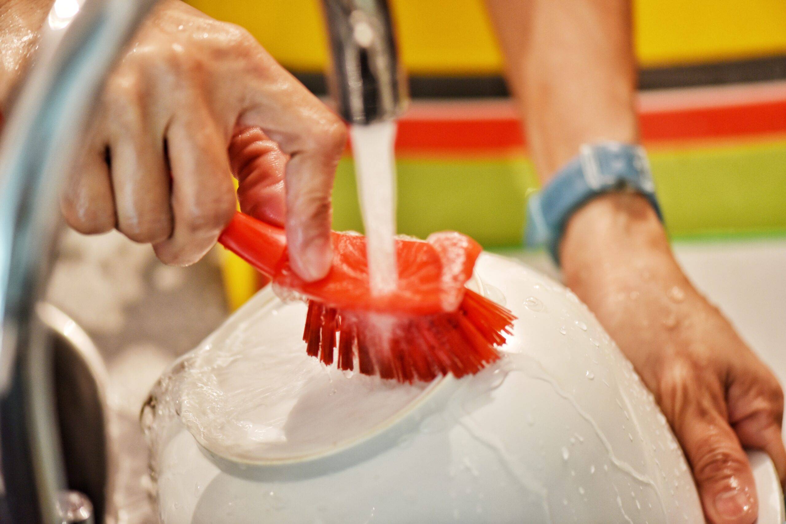 A person cleaning the bottom of a bowl with a red bristled brush.