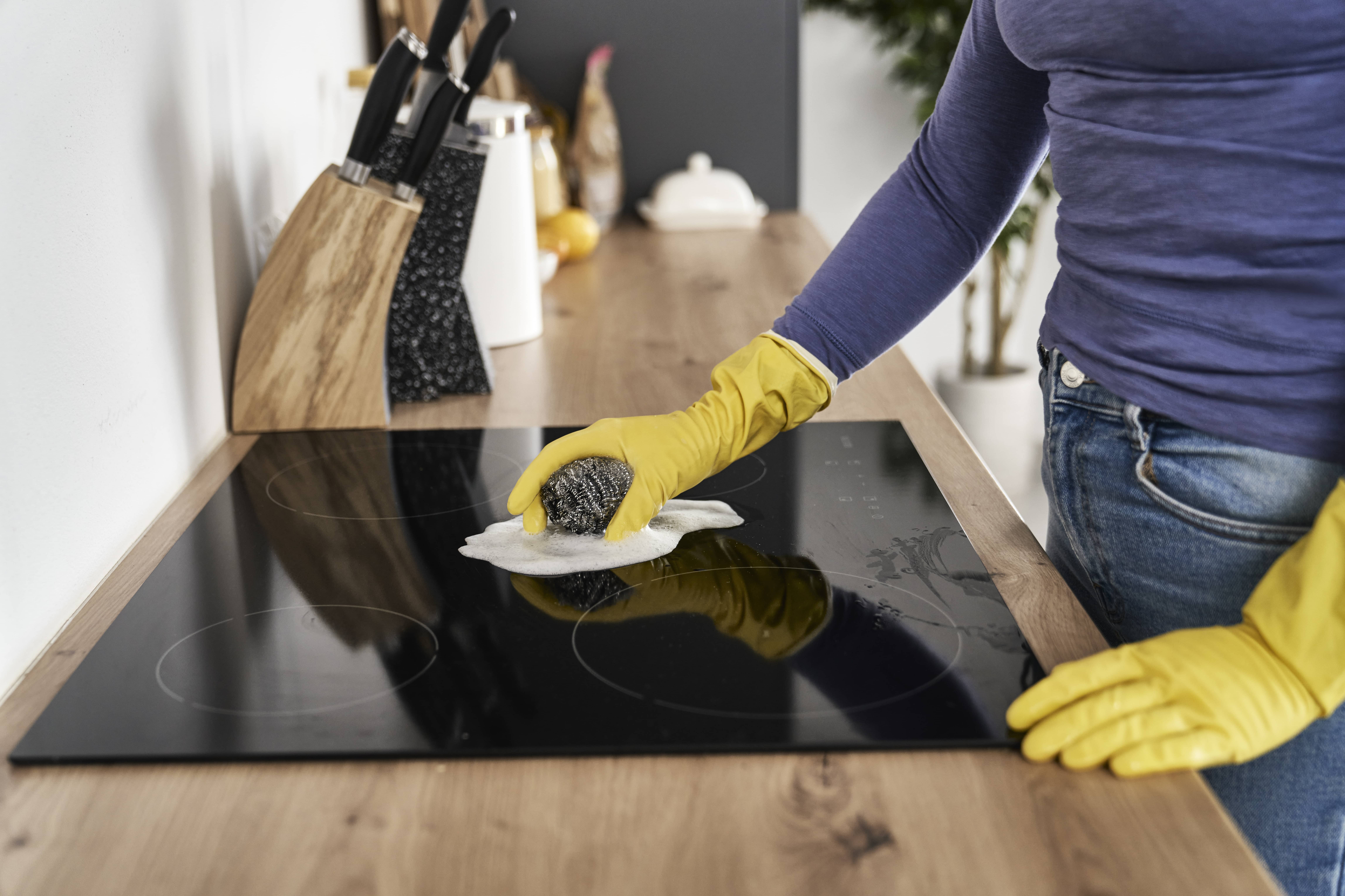 A woman about to clean a stove with a steel wool pad.