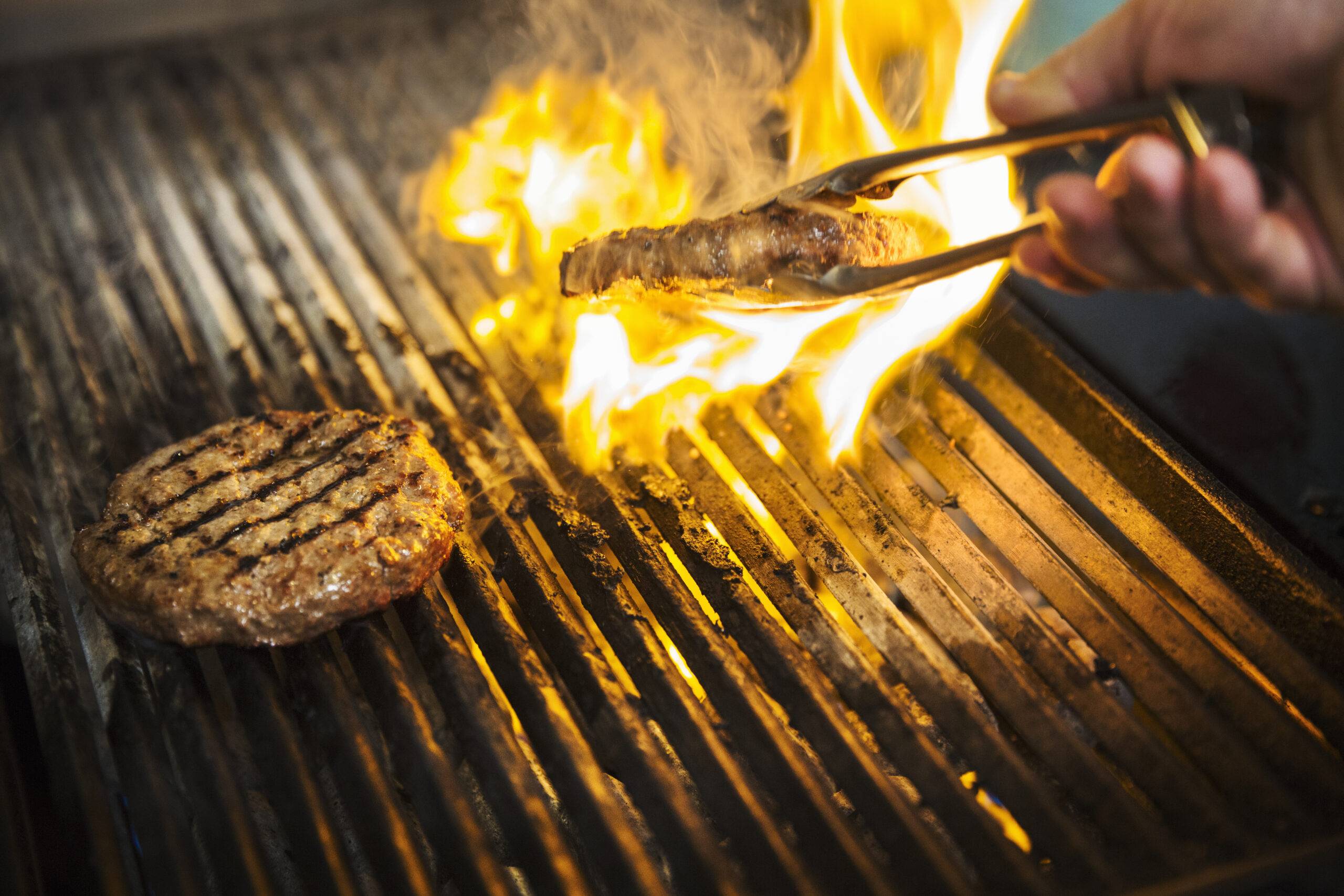 Close up of chef flame grilling a burger on a hot griddle.