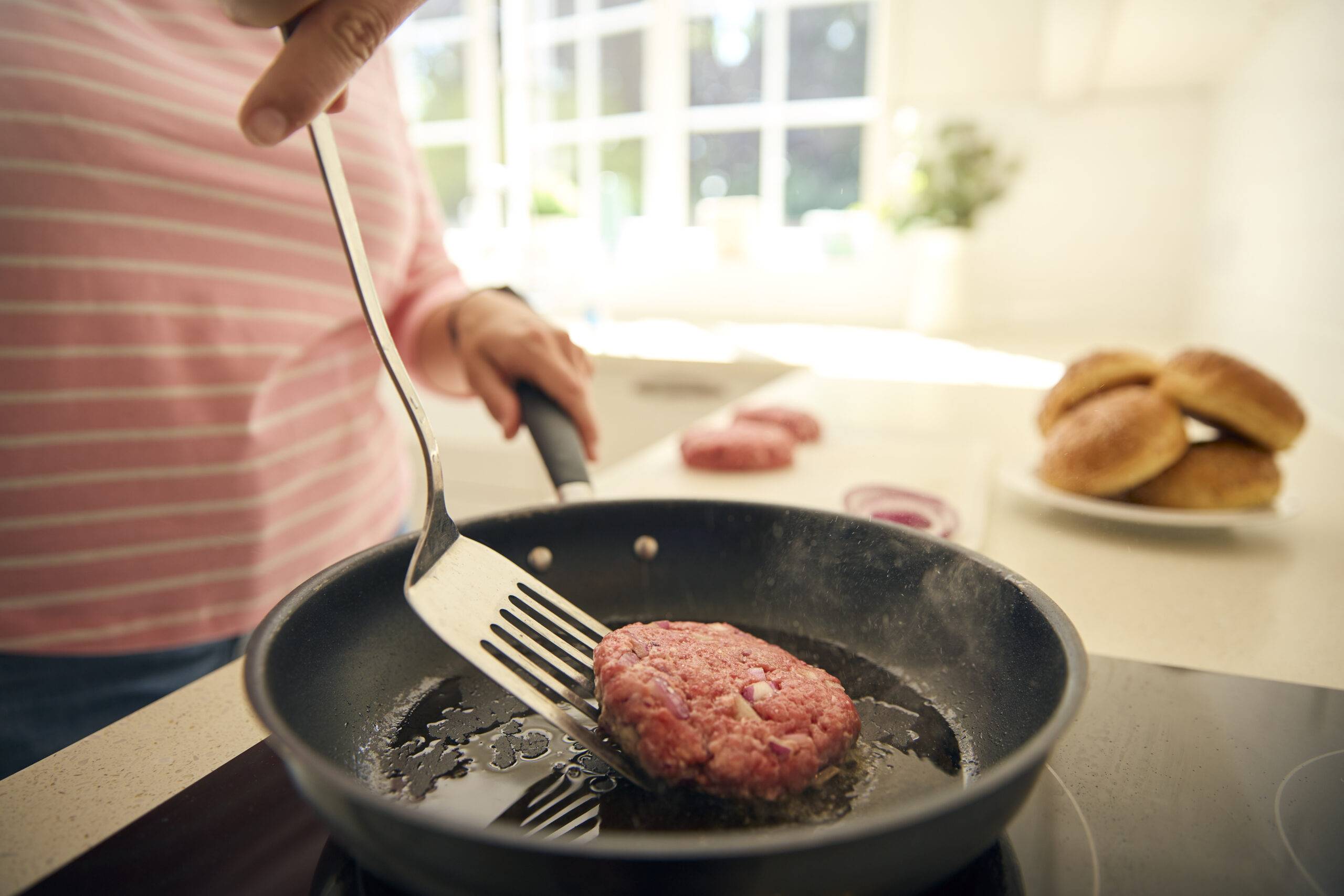 Close Up Of Woman At Home In Kitchen Frying Beef Patty Or Burger In Pan