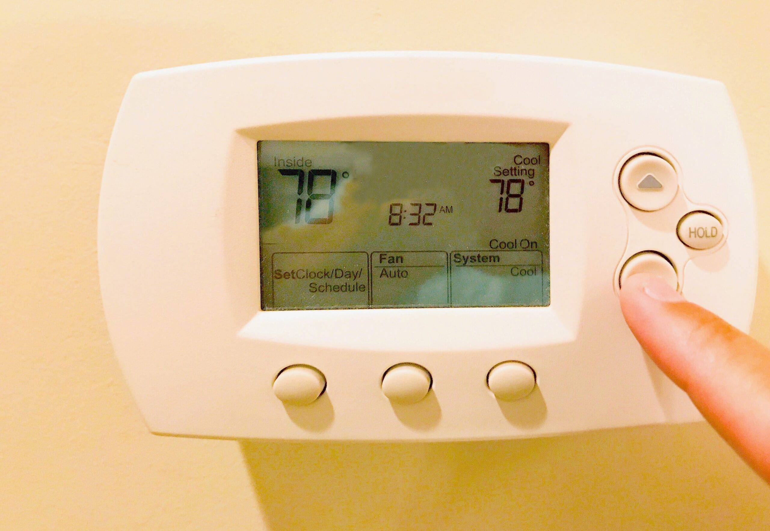 A finger pressing a button on a thermostat.
