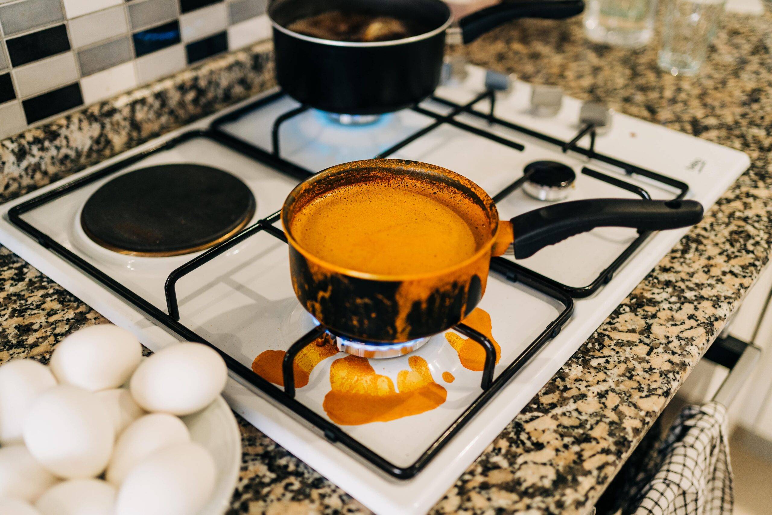 A pot with an orange soup or sauce overboiling and spilling onto the stove.