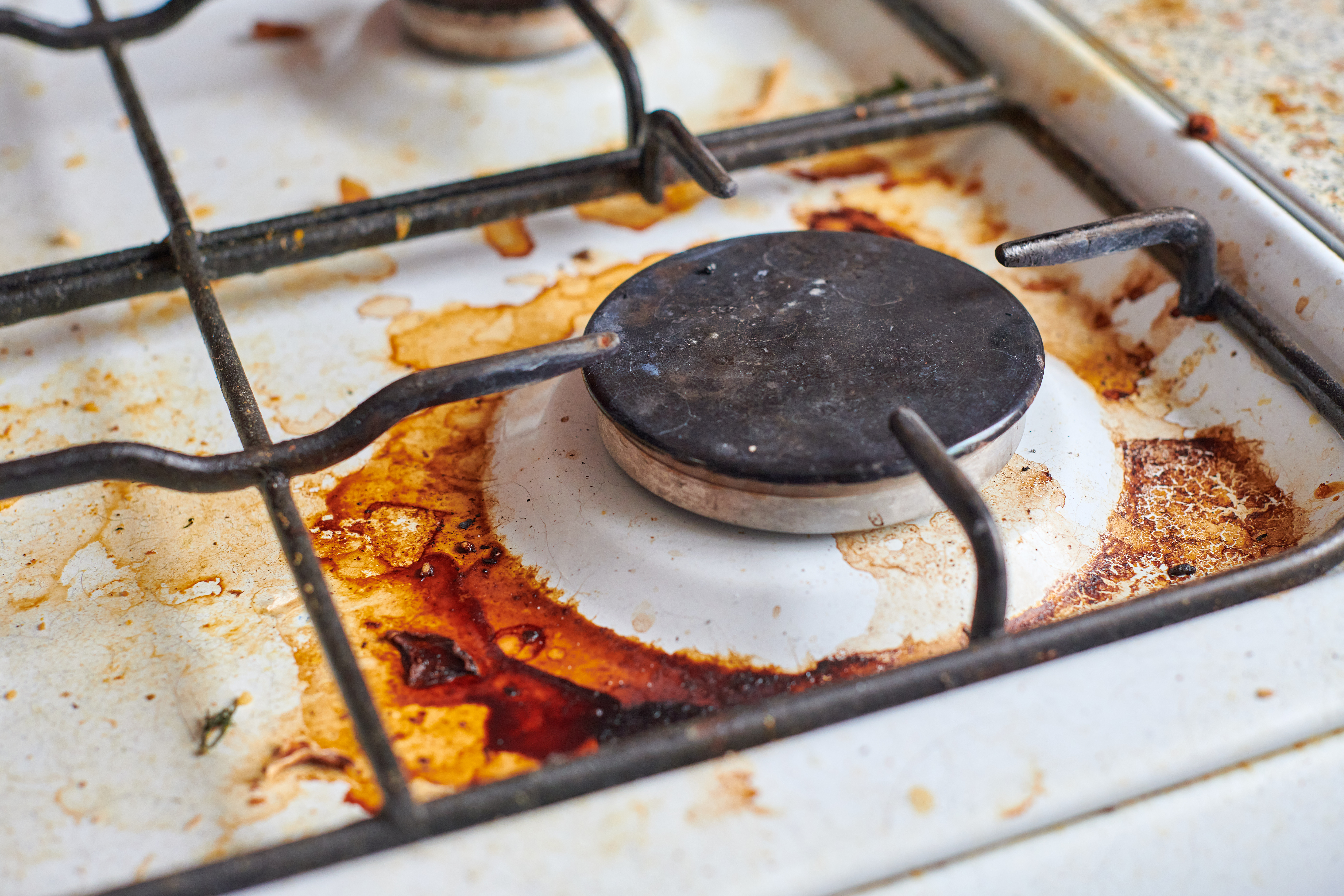 Dirty stove with food leftovers. Unclean gas kitchen cooktop with greasy spots, old fat stains, fry spots and oil splatters.