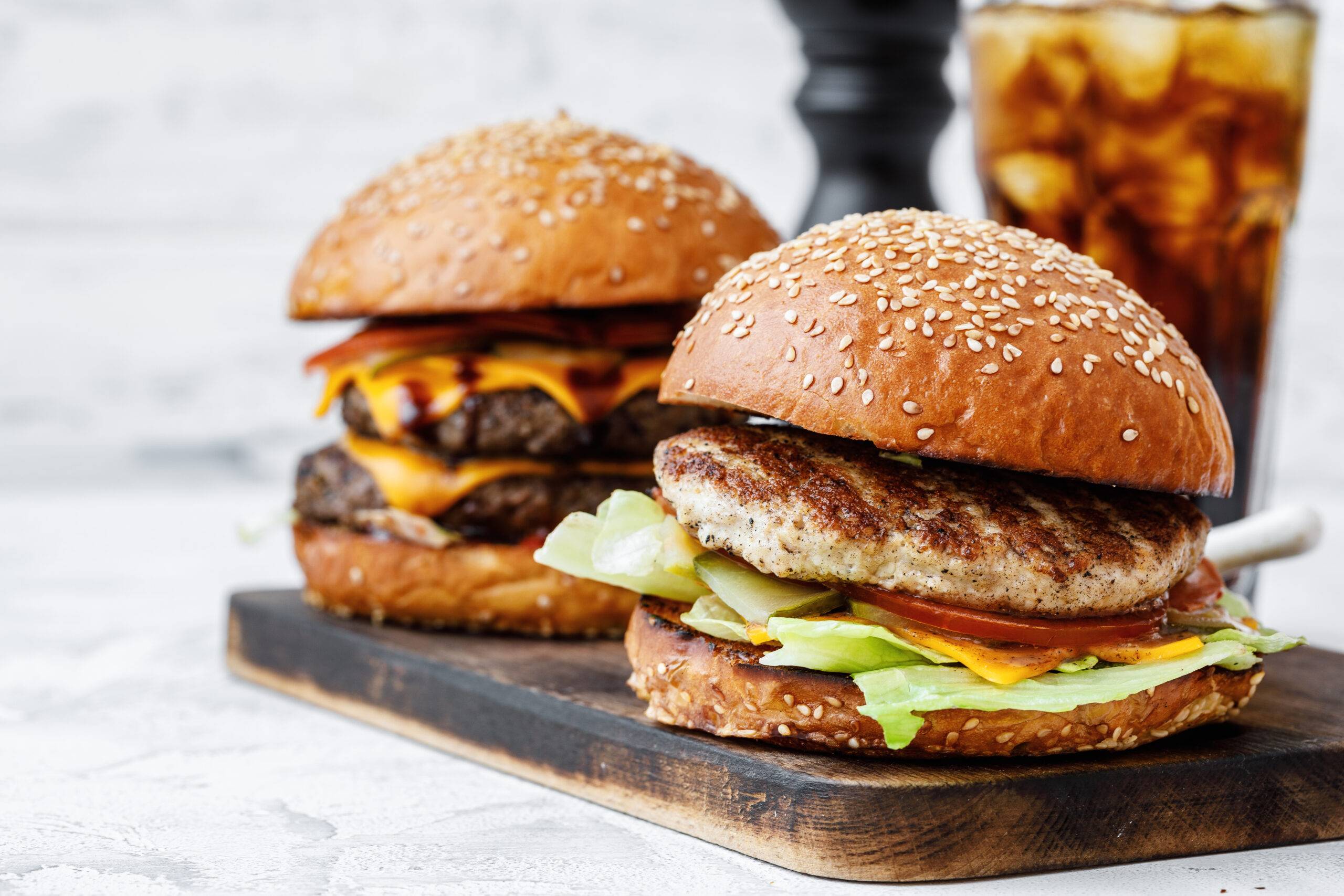 Freshly cooked burger on wooden board on light background, front view