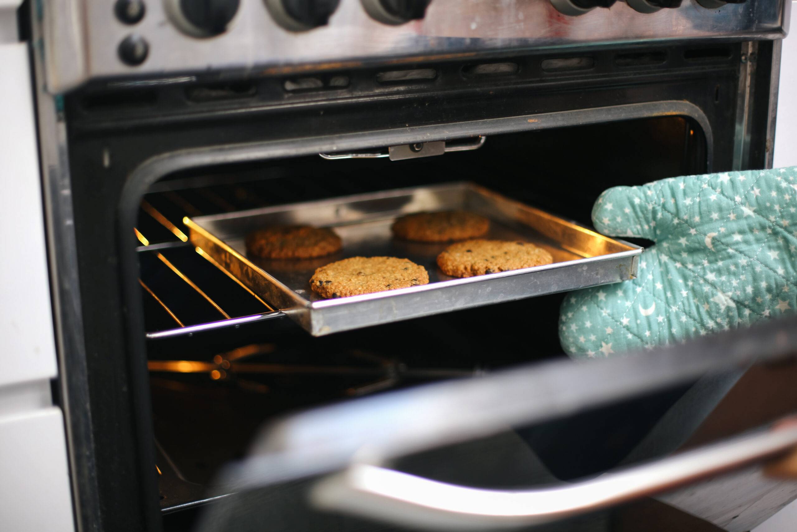 An oven mitt wearing hand putting a tray of burgers into the oven.