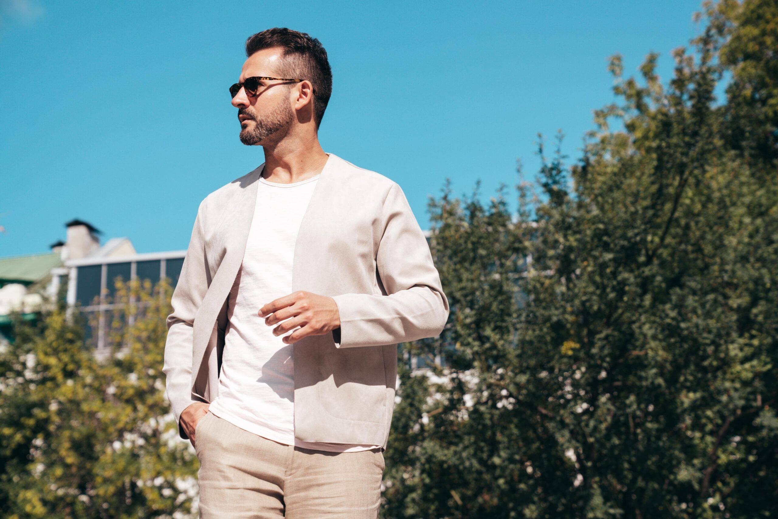 A handsome man in neutral clothing standing outdoors with a drink.