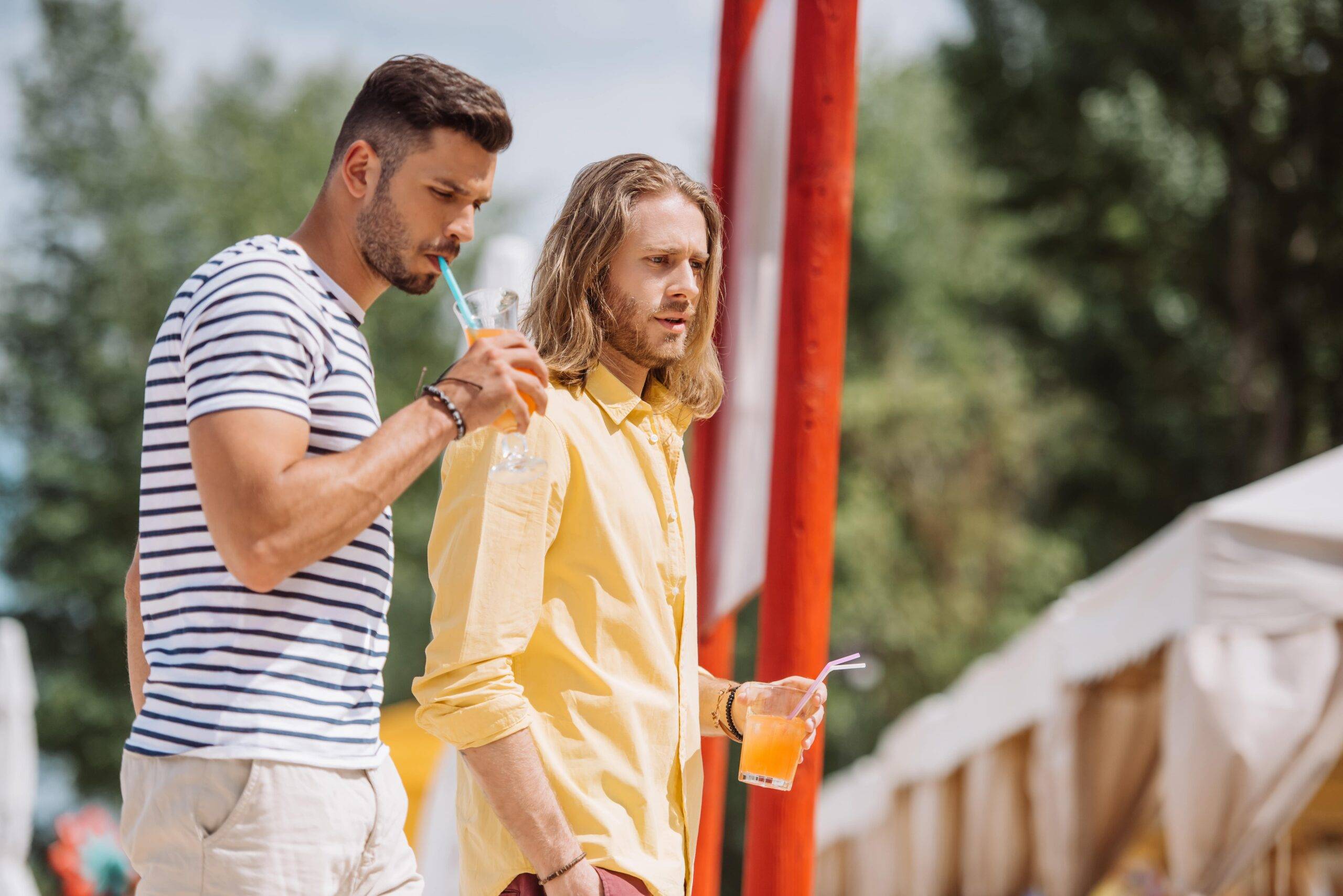 Two young men holding summer drinks, watching something out of frame.