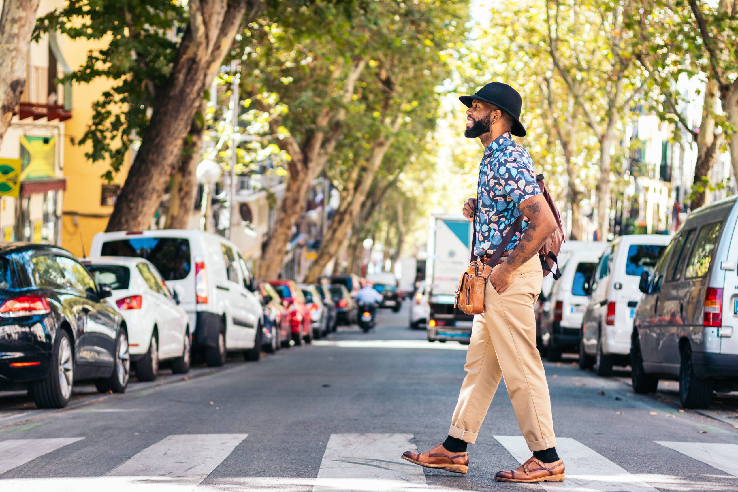 Stylish black man with alternative hipster look walking through the streets of a city on a sunny summer day. he smiles happily