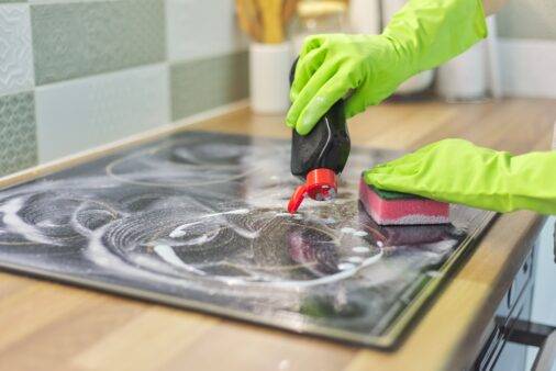 Woman hands in gloves cleans kitchen electric ceramic hob with sponge and detergent
