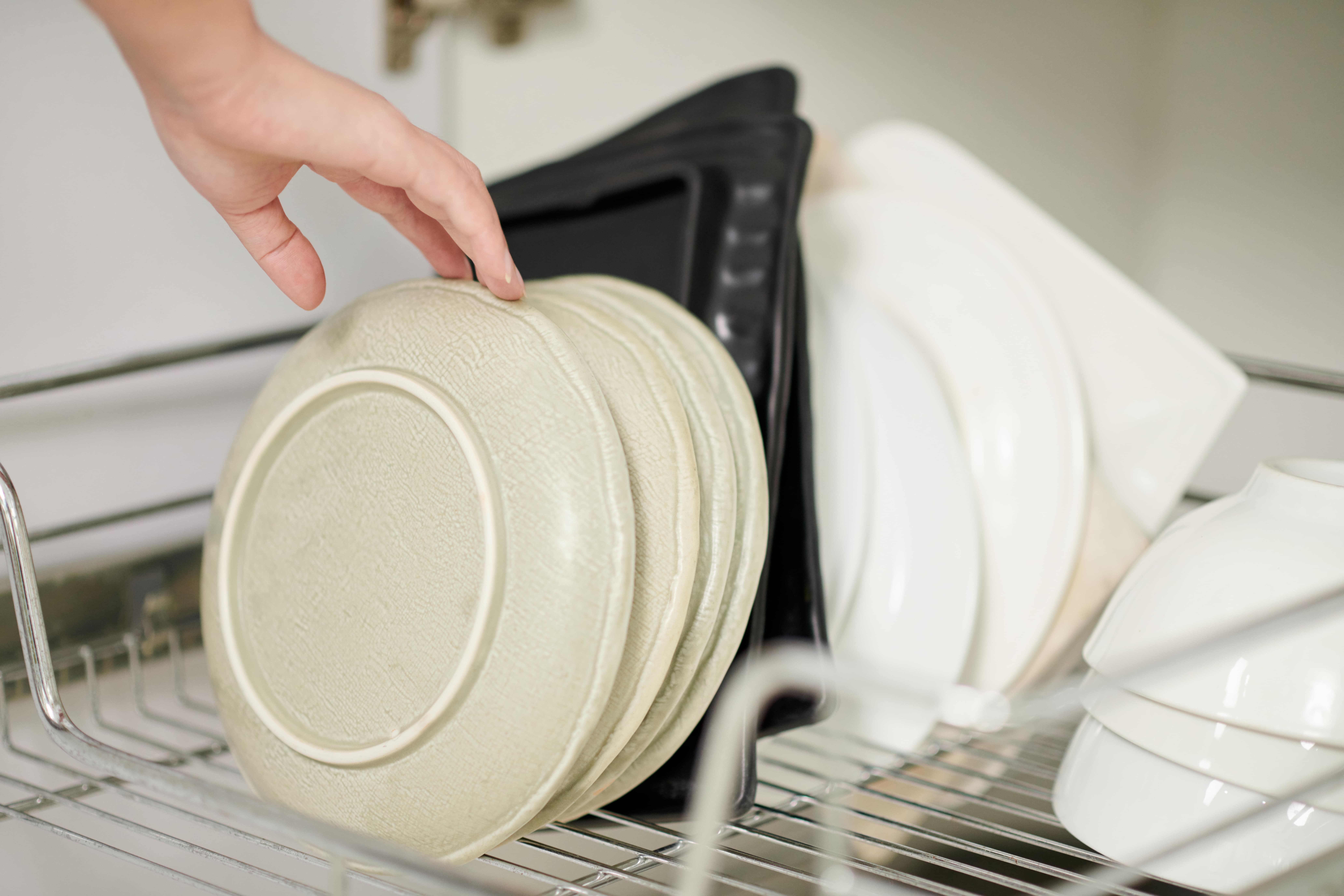 A person stacking dishes in a drying rack.