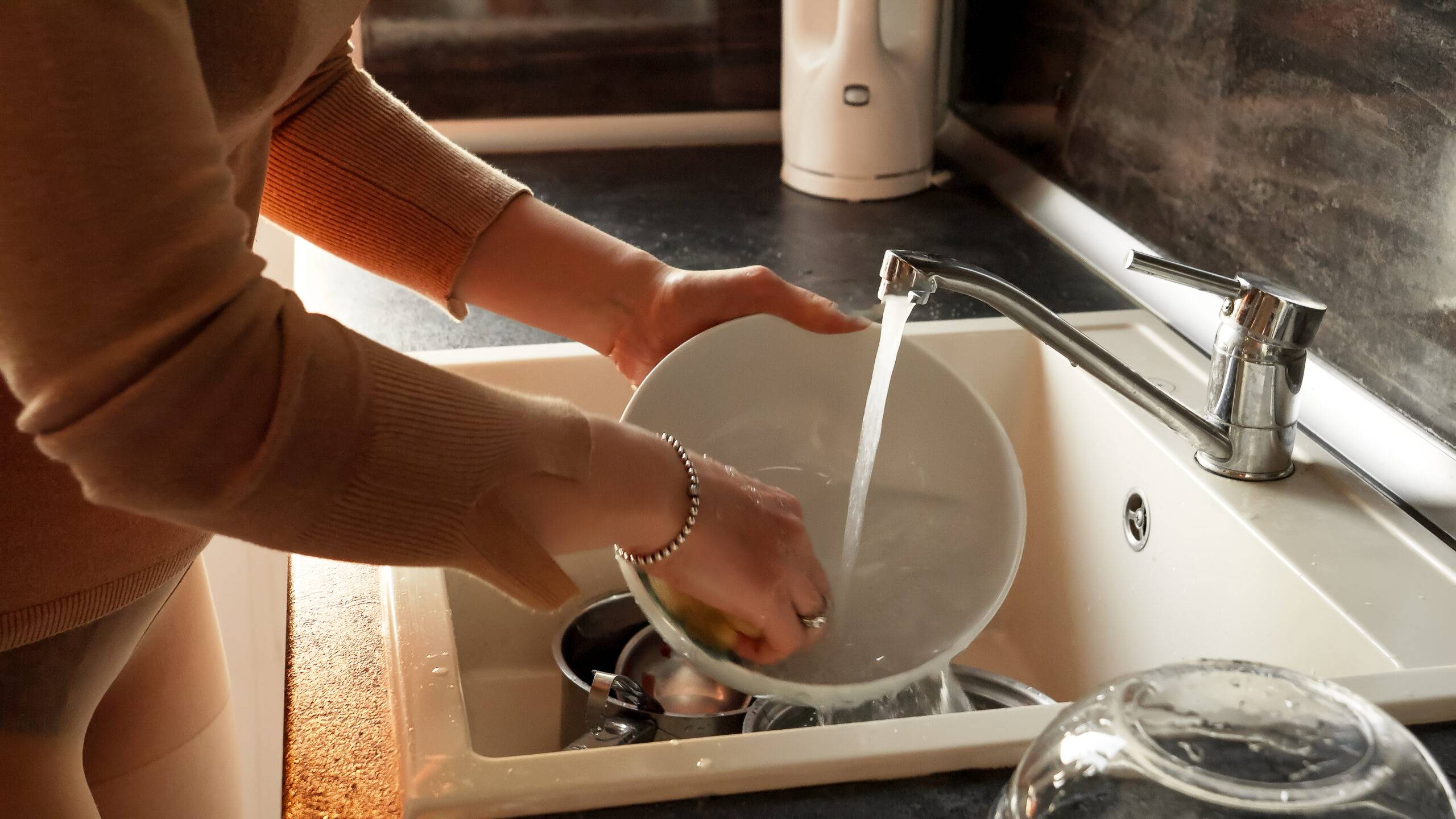 Young housewife washing dishes and bowls on kitchen. Housewife working, domestic chores, doing housework.