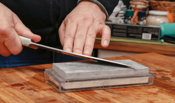 A closer photo of someone using a whetstone to sharpen a knife.