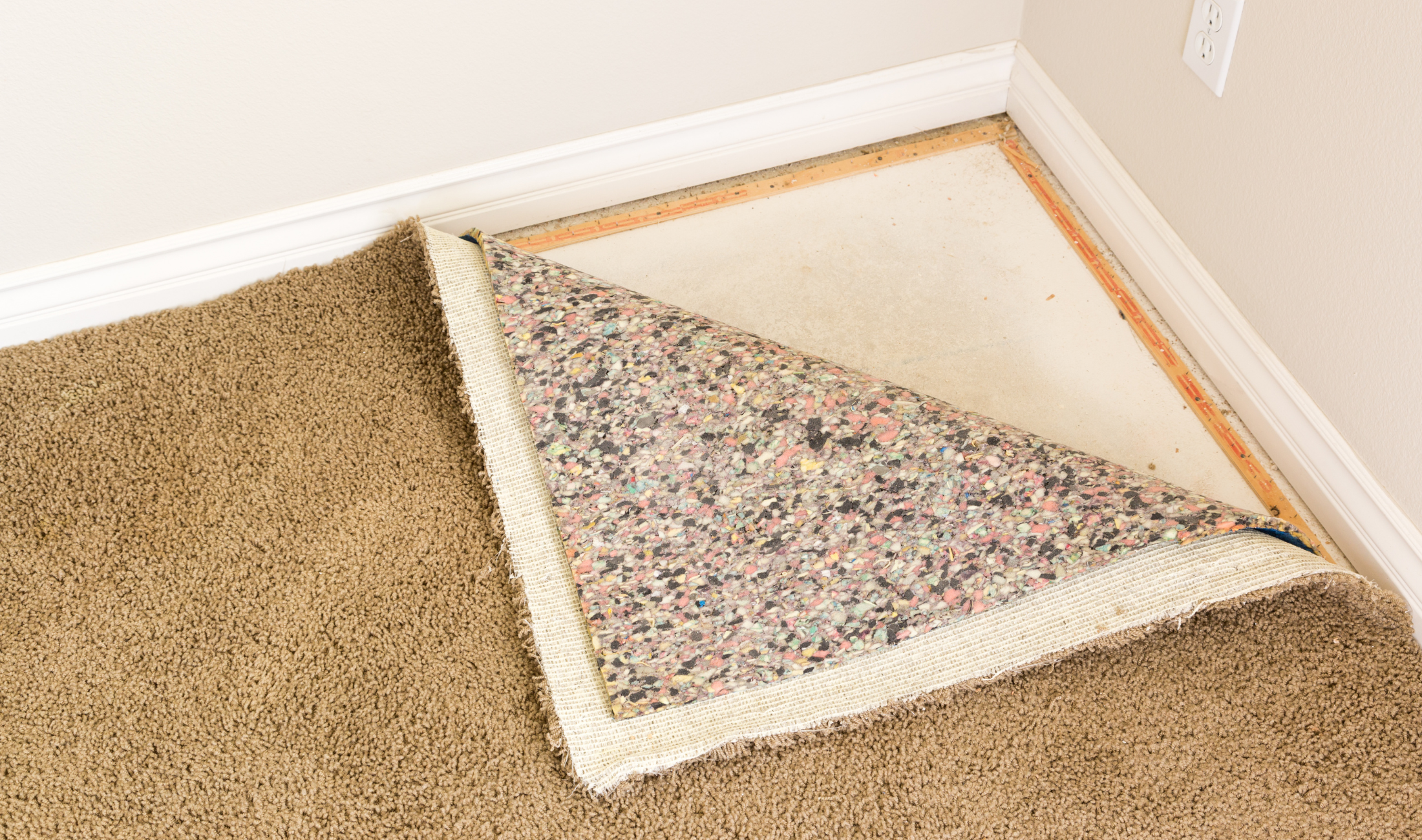 A carpet lifted up in the corner to reveal the subfloor.