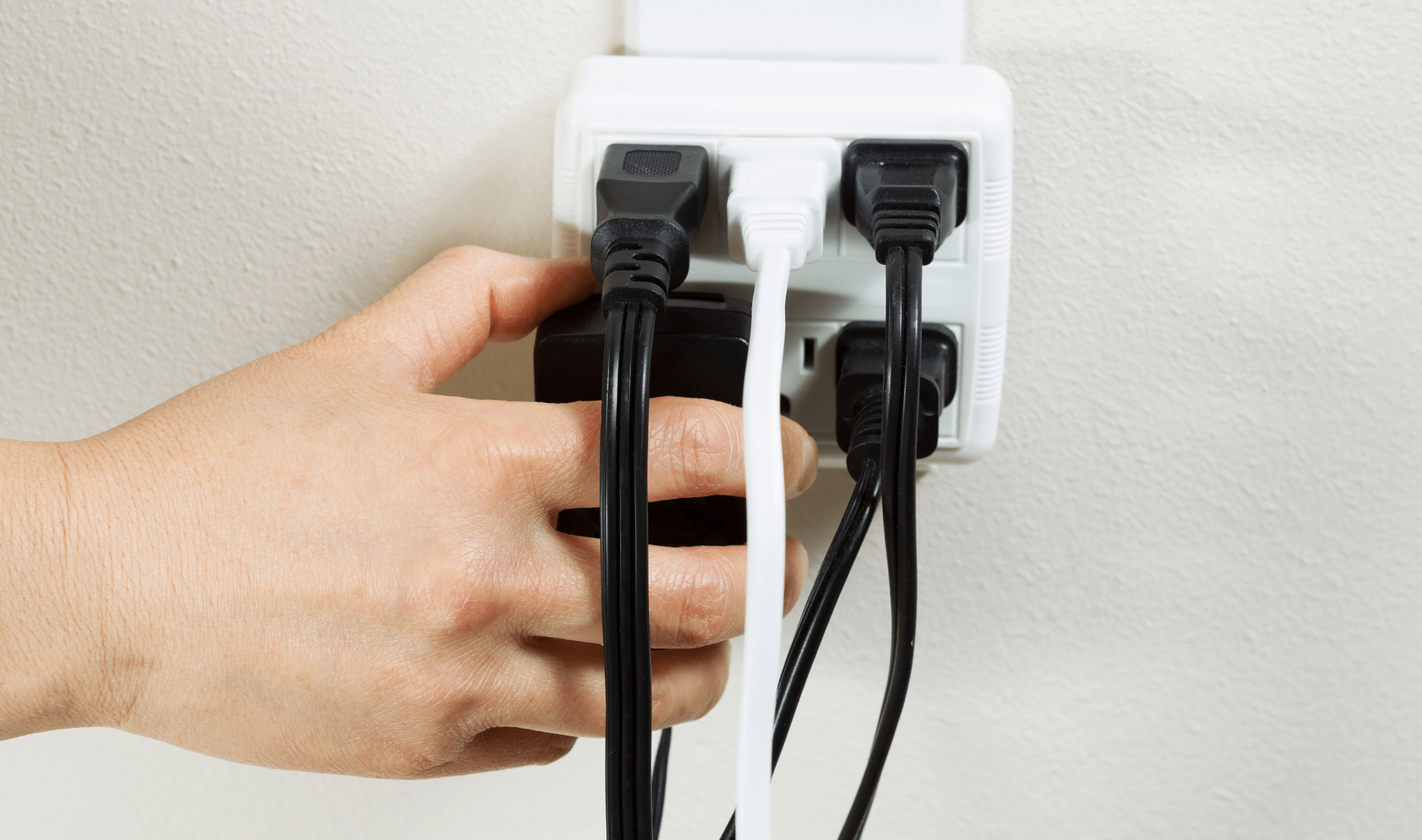 A person plugging another item into an already overloaded outlet.