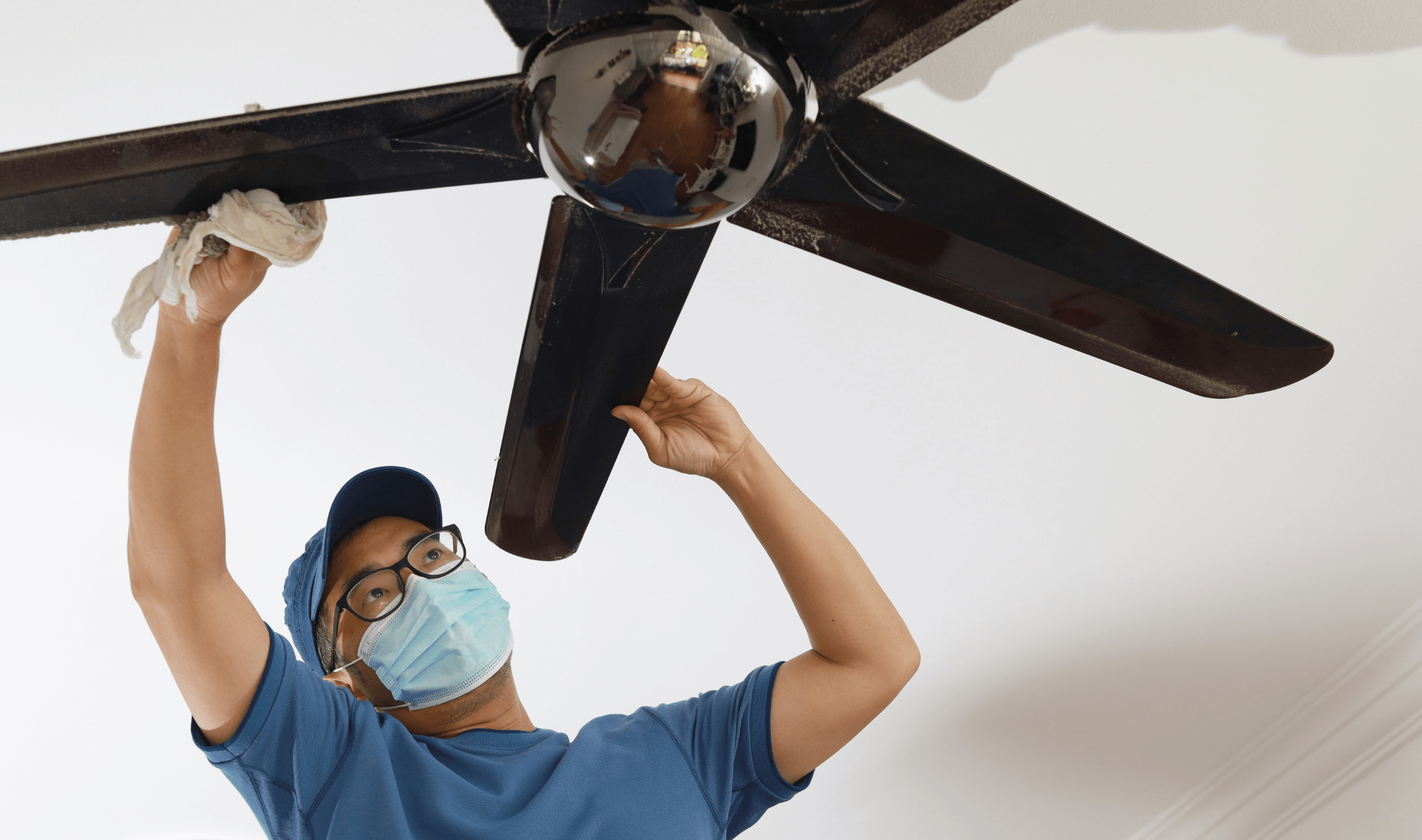 A man cleaning a ceiling fan.