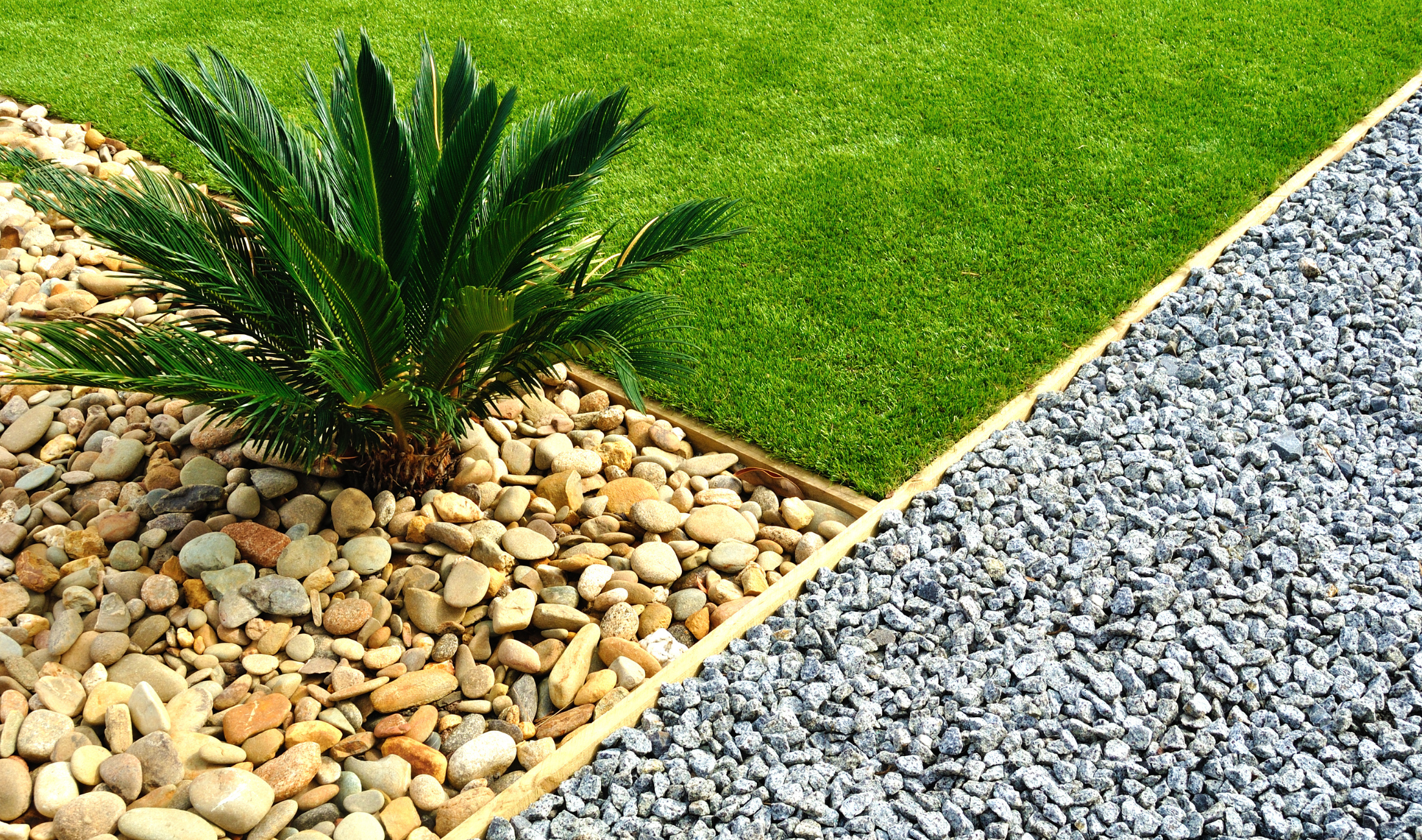 A section of garden that's divided into 3 sections, two with differing types of gravel, one with grass.