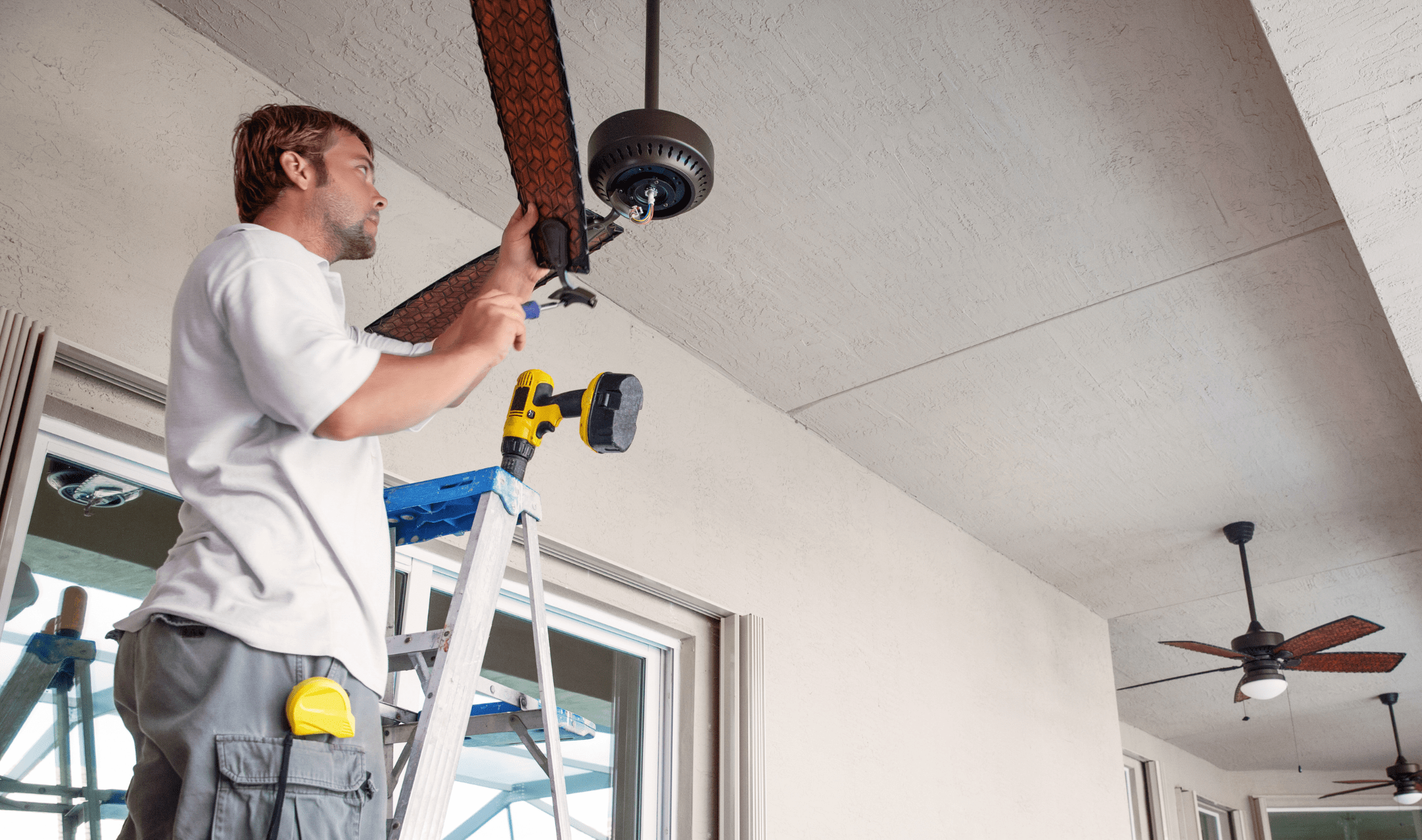 A man up on a ladder, assembling a ceiling fan.