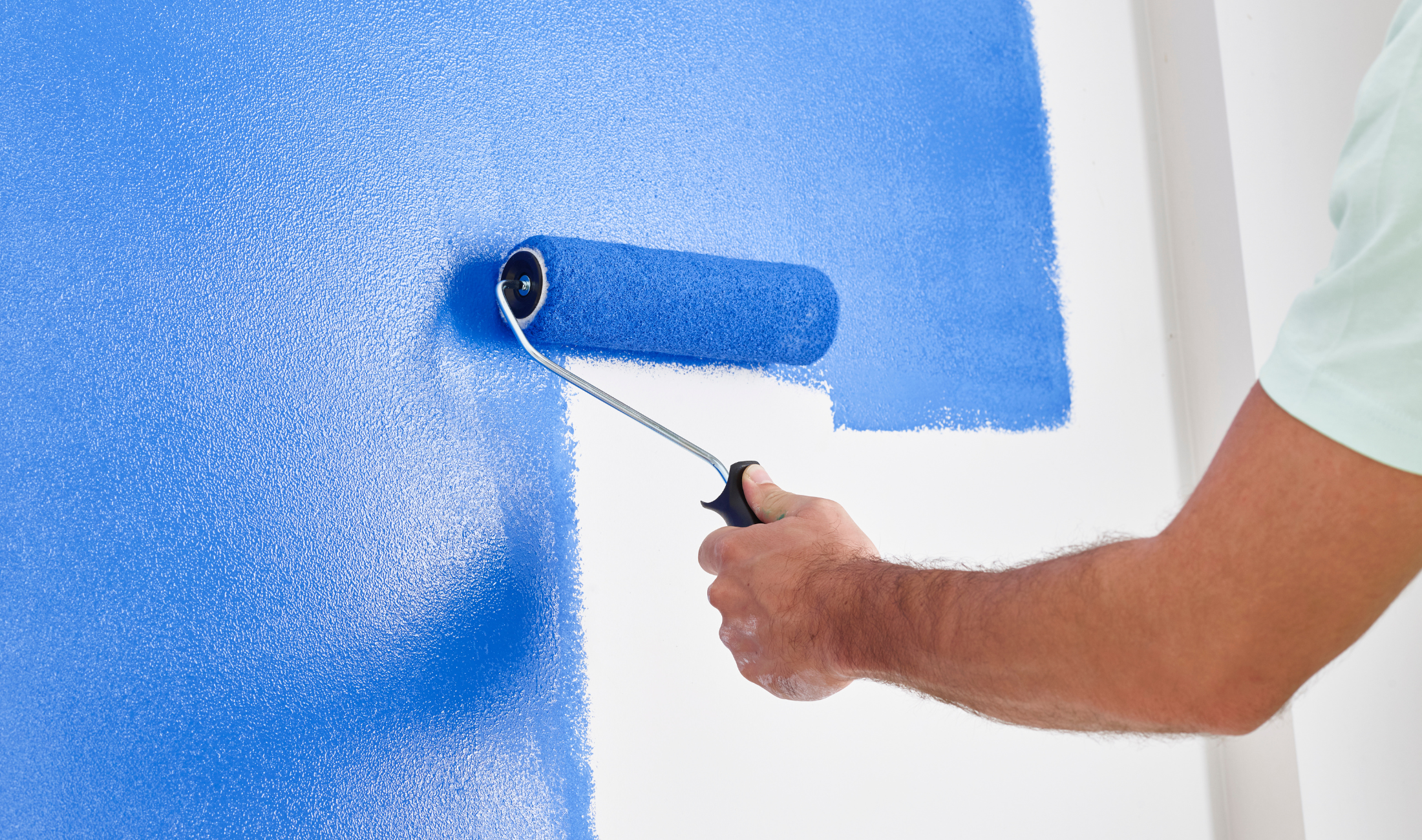A person's hand using a paint roller to paint a wall blue.