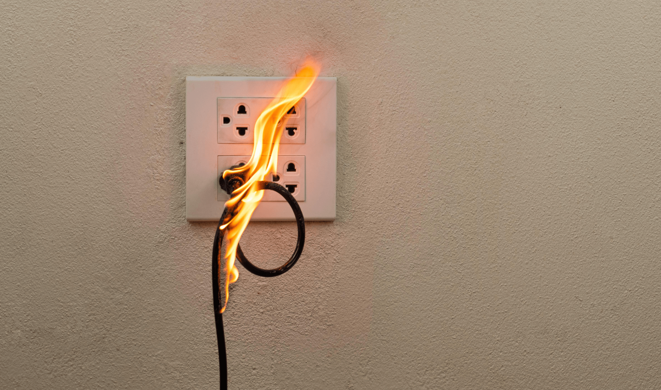 An electrical outlet with a cable plugged in that's on fire.