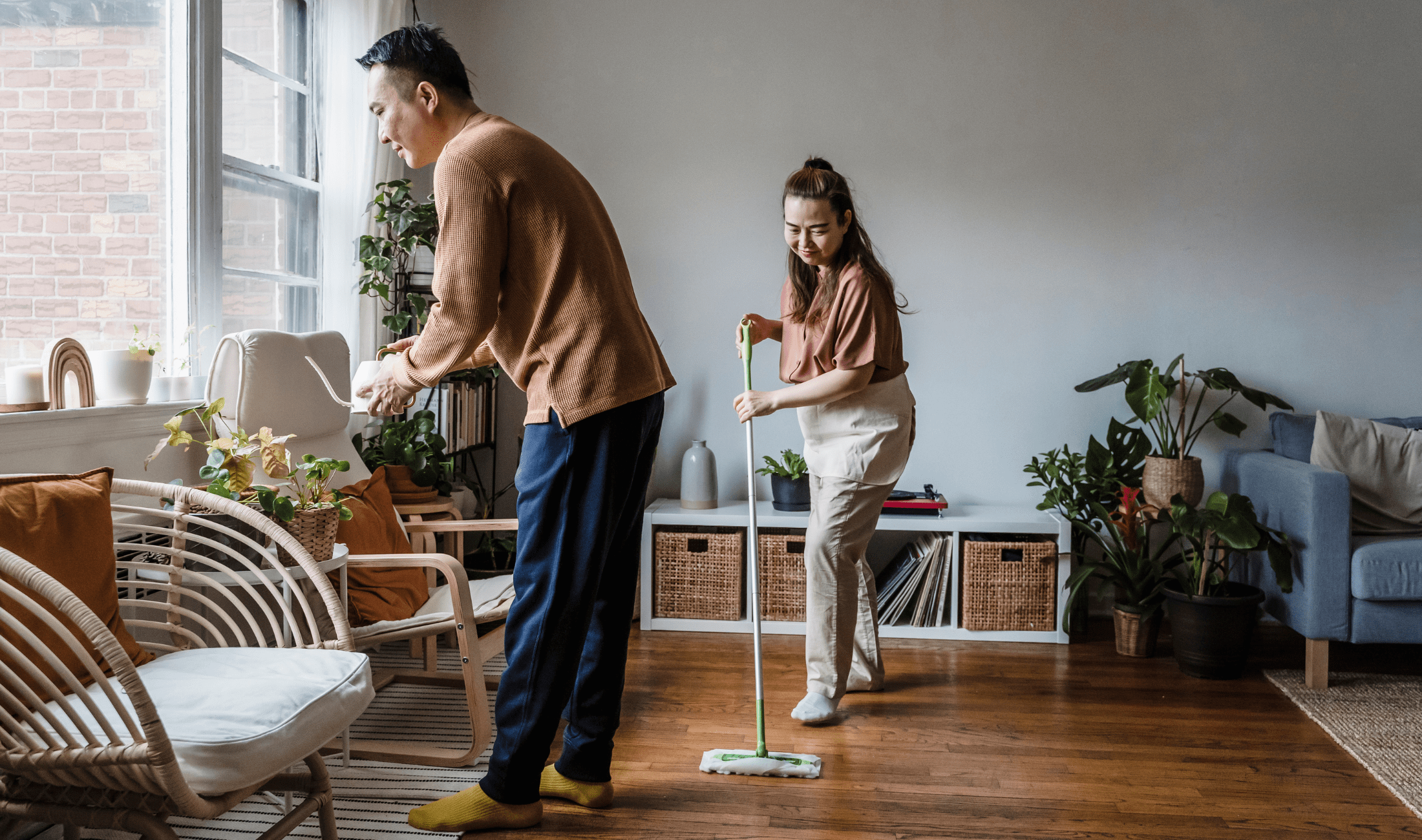 A couple cleaning their living room, the man tidying as the woman cleans.
